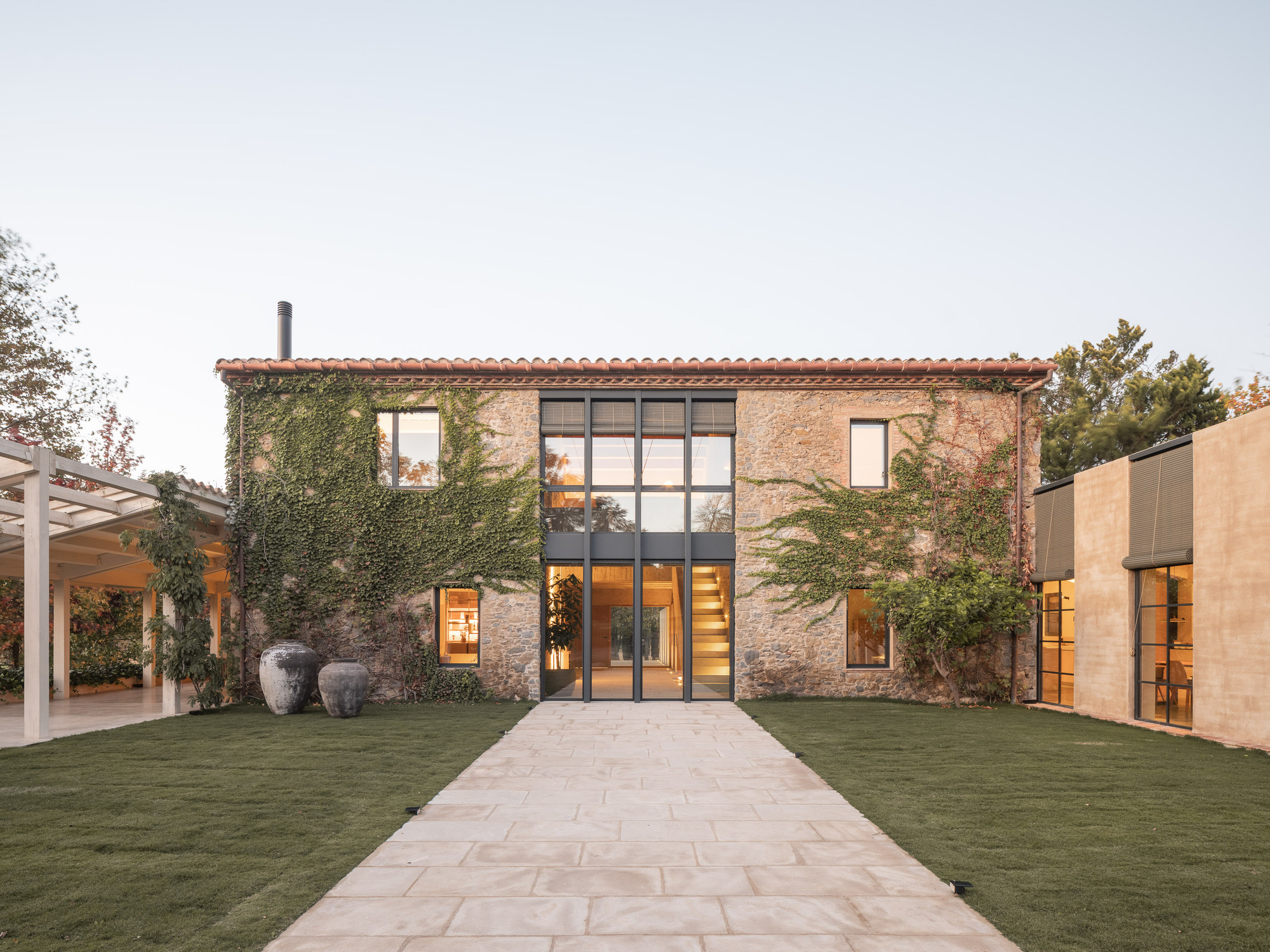 Ivy-covered stone facade with gridded steel-framed glazing illuminated from within at twilight