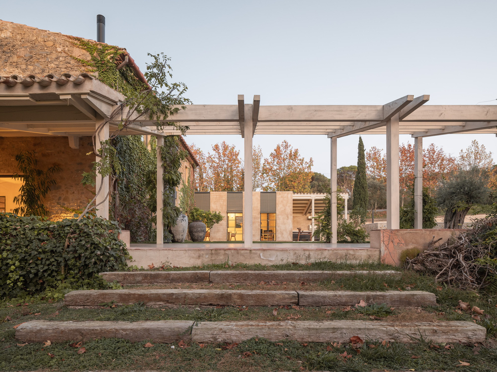 Timber pergola shading stepped stone terrace with view to ivy-clad building and sandstone wing beyond