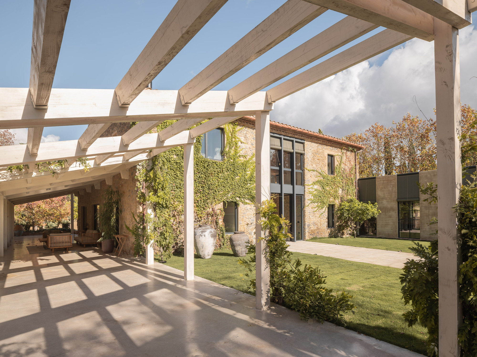 Courtyard view through timber pergola beams casting shadows on paving at midday