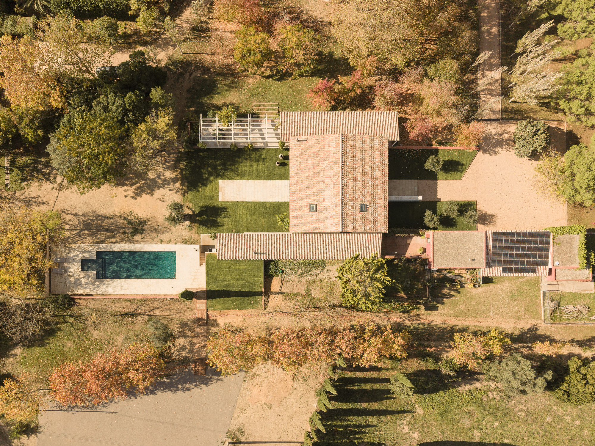Aerial view of the compound showing brick tower, swimming pool, and slatted canopies among autumn trees