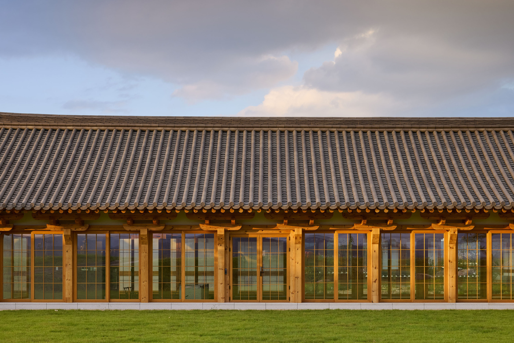 Exterior facade with repeating timber-framed glazed doors beneath a sweeping tile roof at dusk