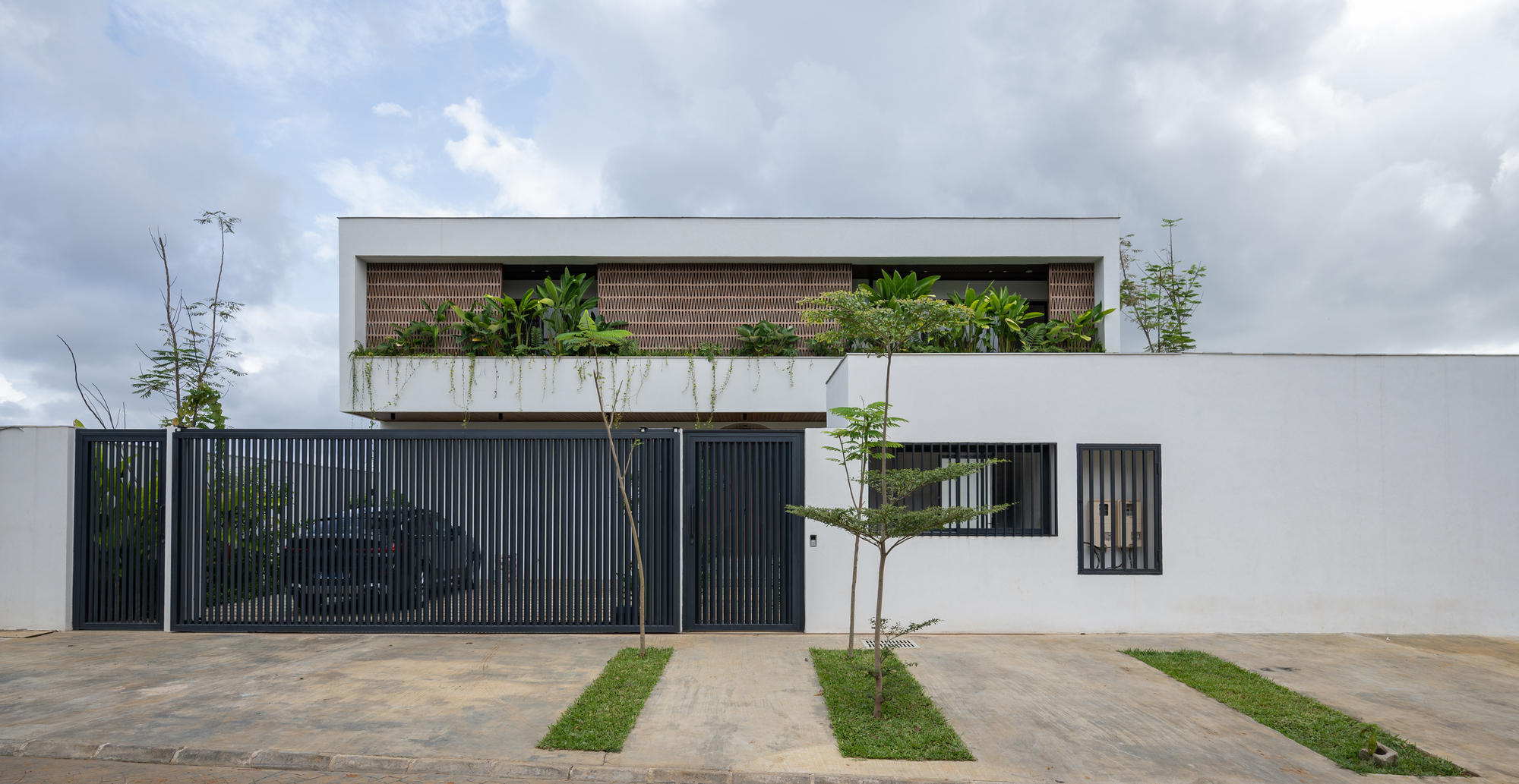 Street facade with dark vertical metal gate and planted terrace above under overcast afternoon light