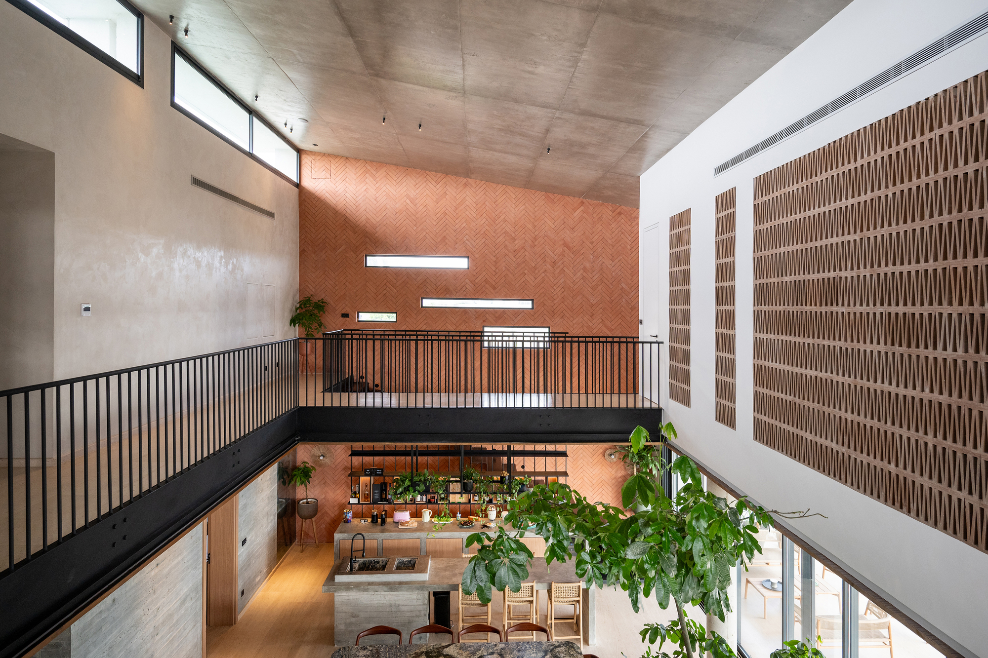 Double-height living space with herringbone brick wall and steel balcony overlooking furnishings and potted plants below