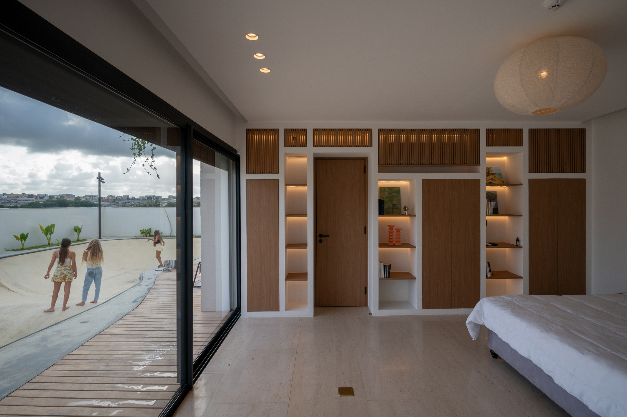 Bedroom with built-in timber storage wall and glass doors opening to wooden deck at dusk