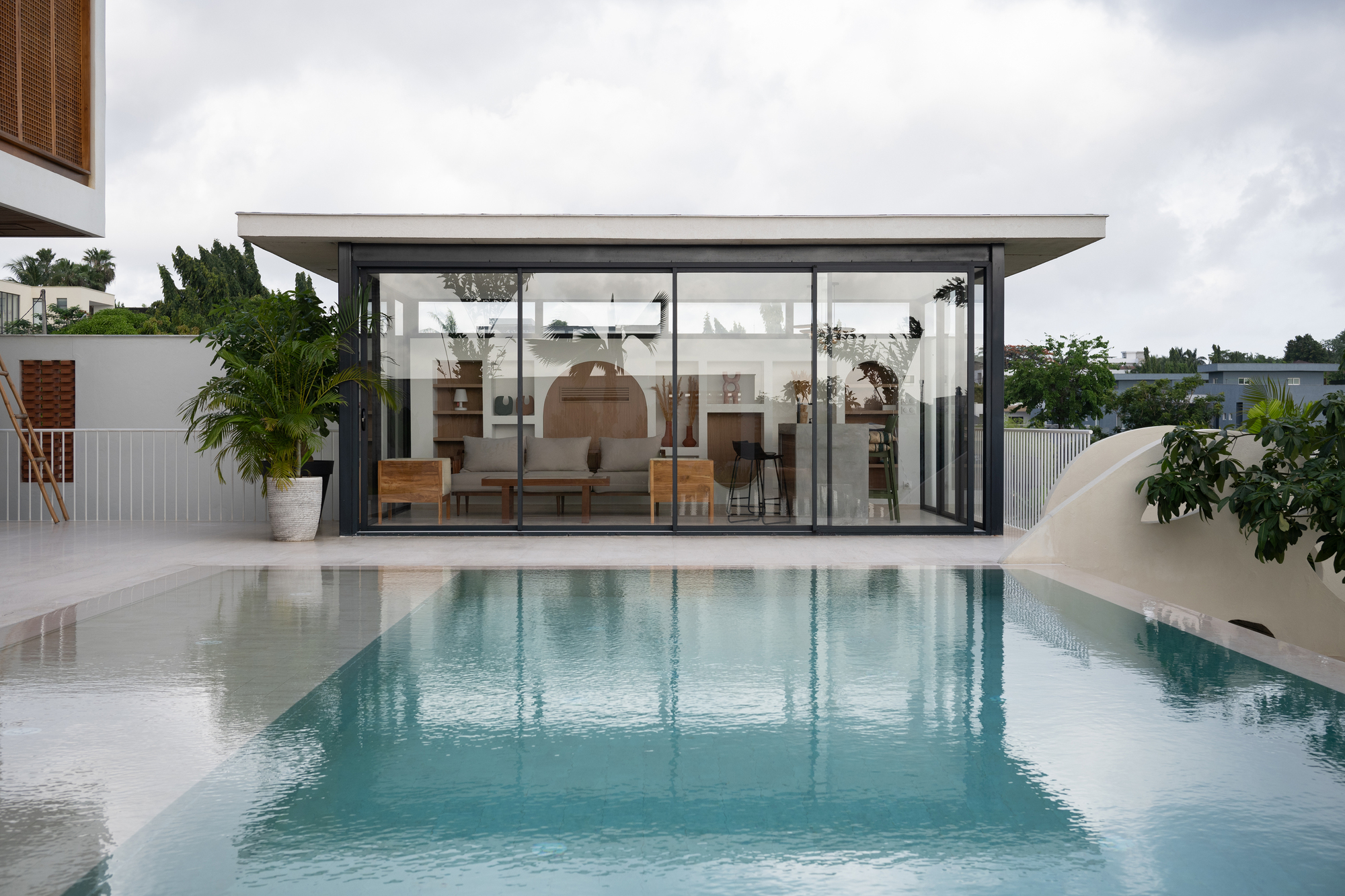 Rooftop pool reflecting the glass-walled pavilion and potted palms on an overcast day