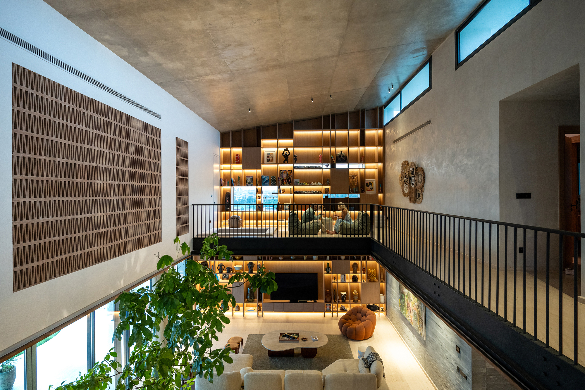 Double-height living room with exposed concrete ceiling and backlit timber shelving above the balcony