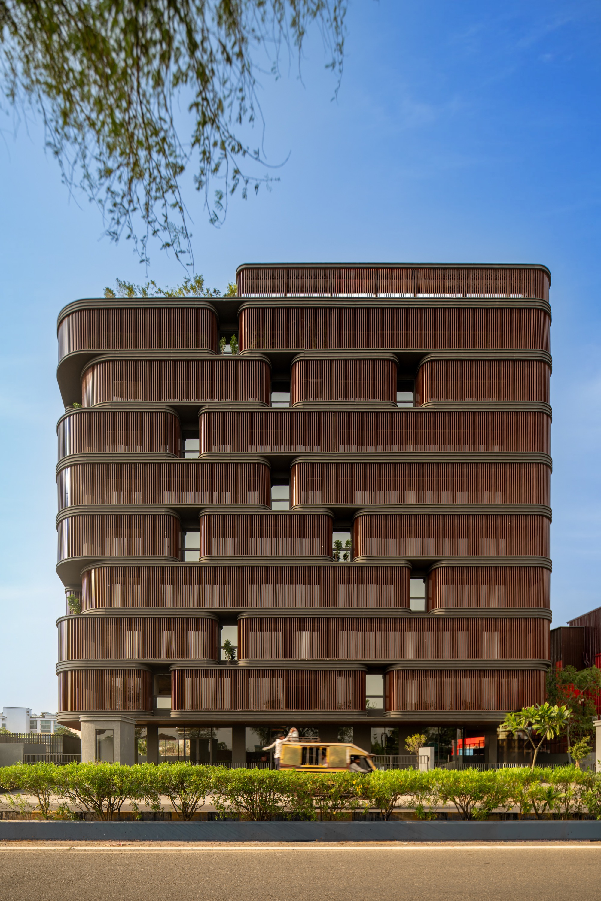 Street view of the residential building with rounded balconies and willow branches overhead
