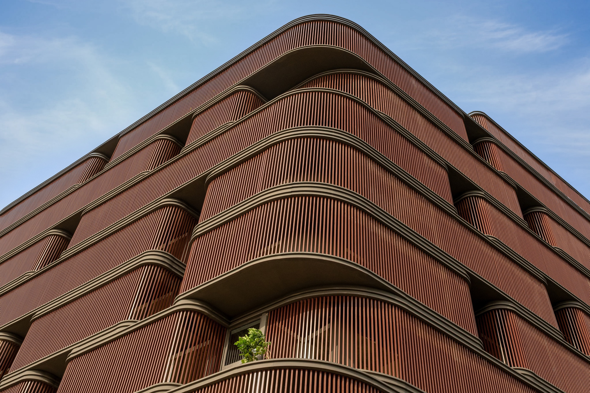 Corner view of the building showing curved timber-clad balconies and recessed terraces