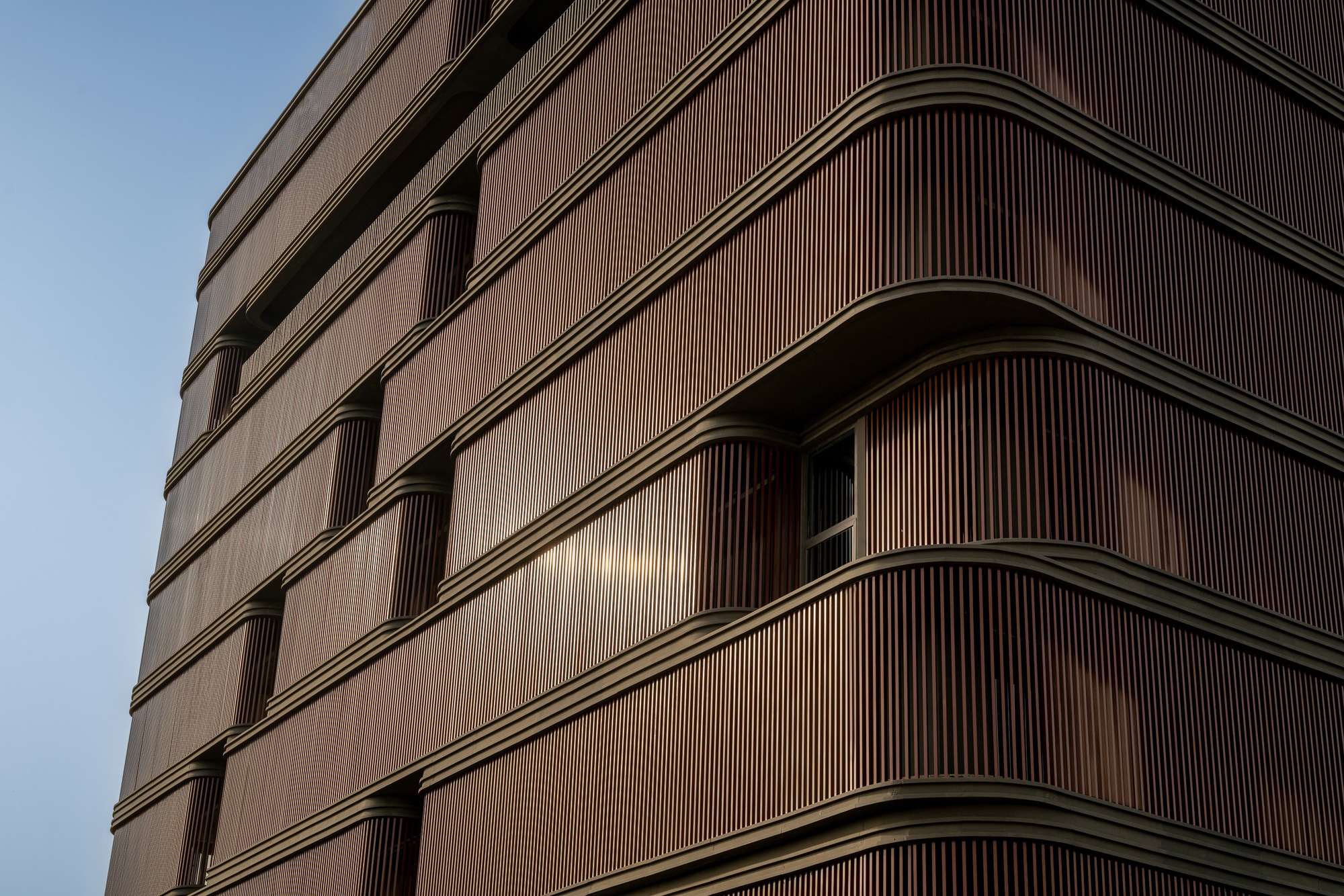 Facade detail of the timber louvered screens at dusk with recessed balcony openings