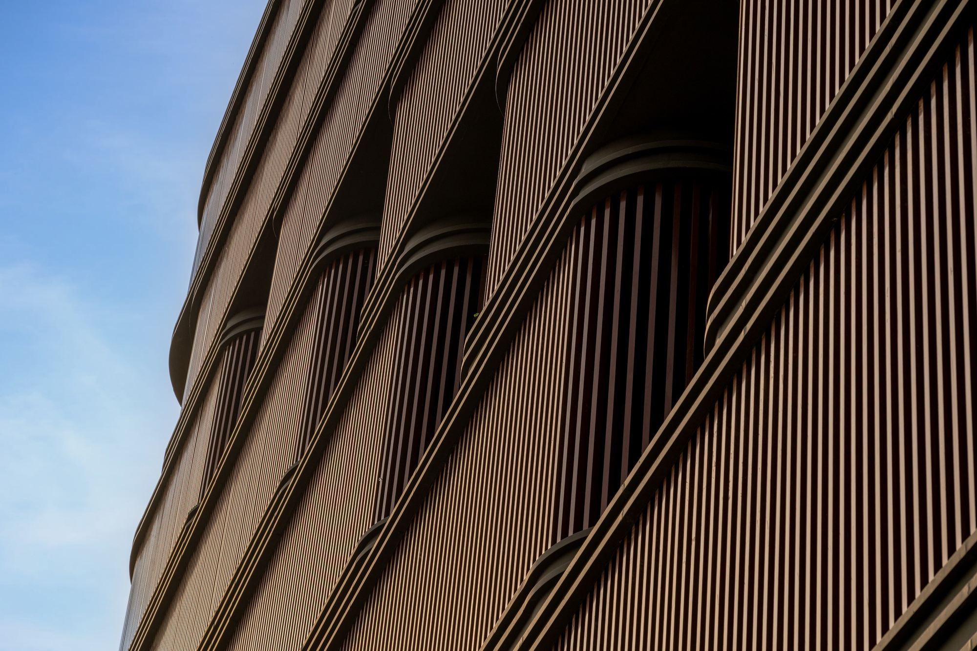 Close-up of the curved facade with vertical bronze-toned louvers creating arched openings against a blue sky
