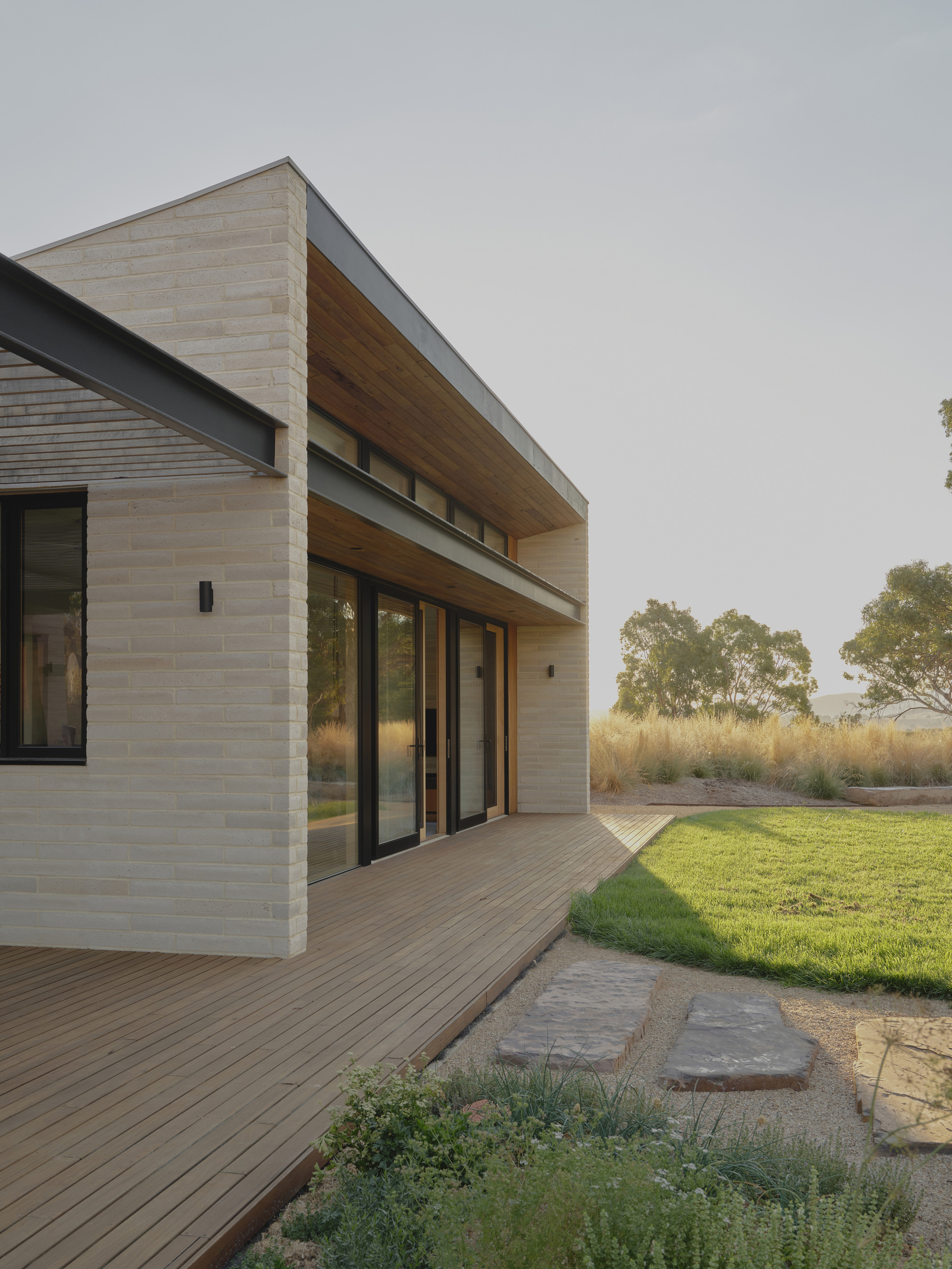 Timber deck and cantilevered overhang adjoining a mown lawn with stepping stones through gravel