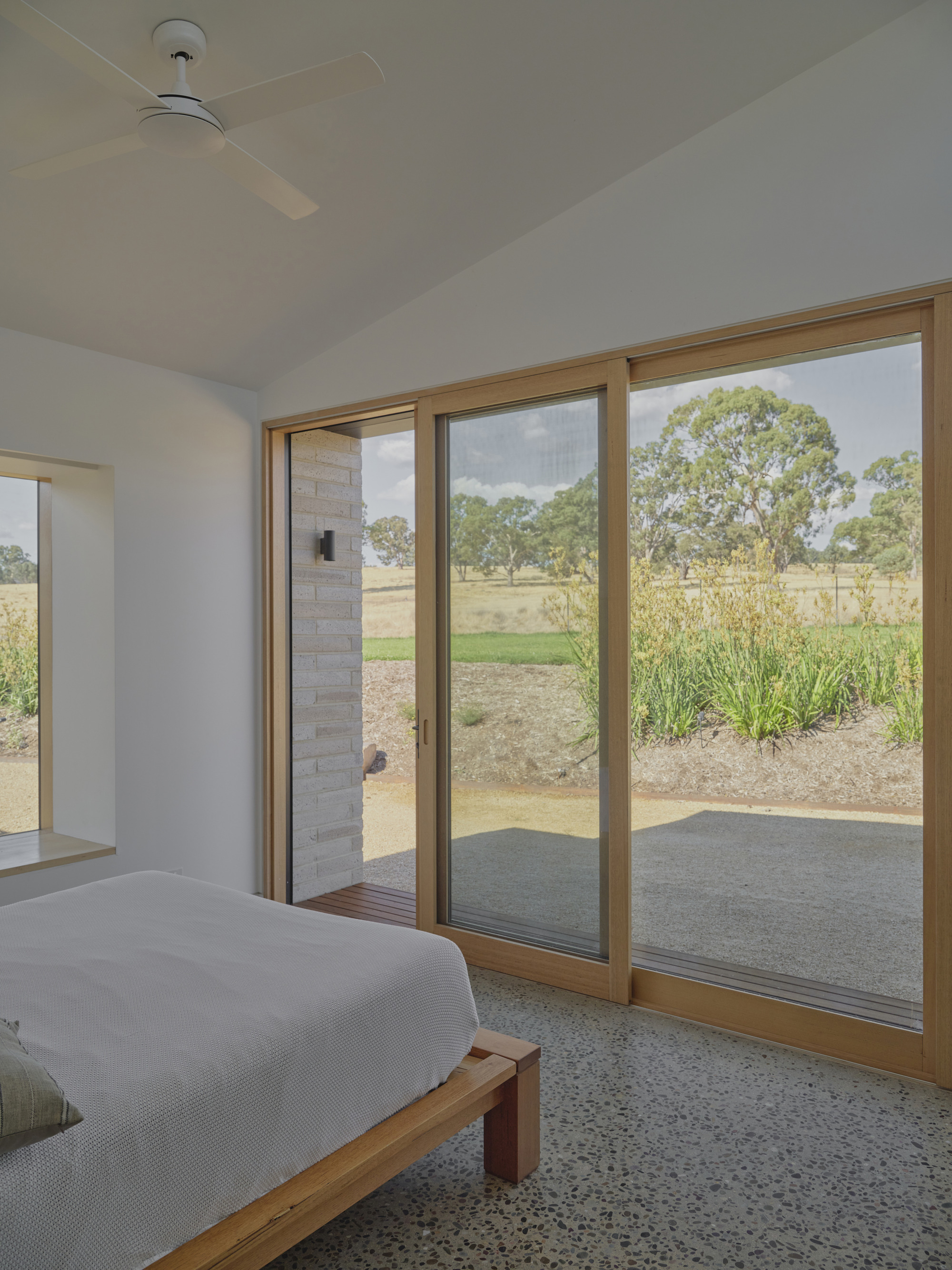Bedroom with timber-framed sliding doors opening to a terrazzo floor and grassland beyond