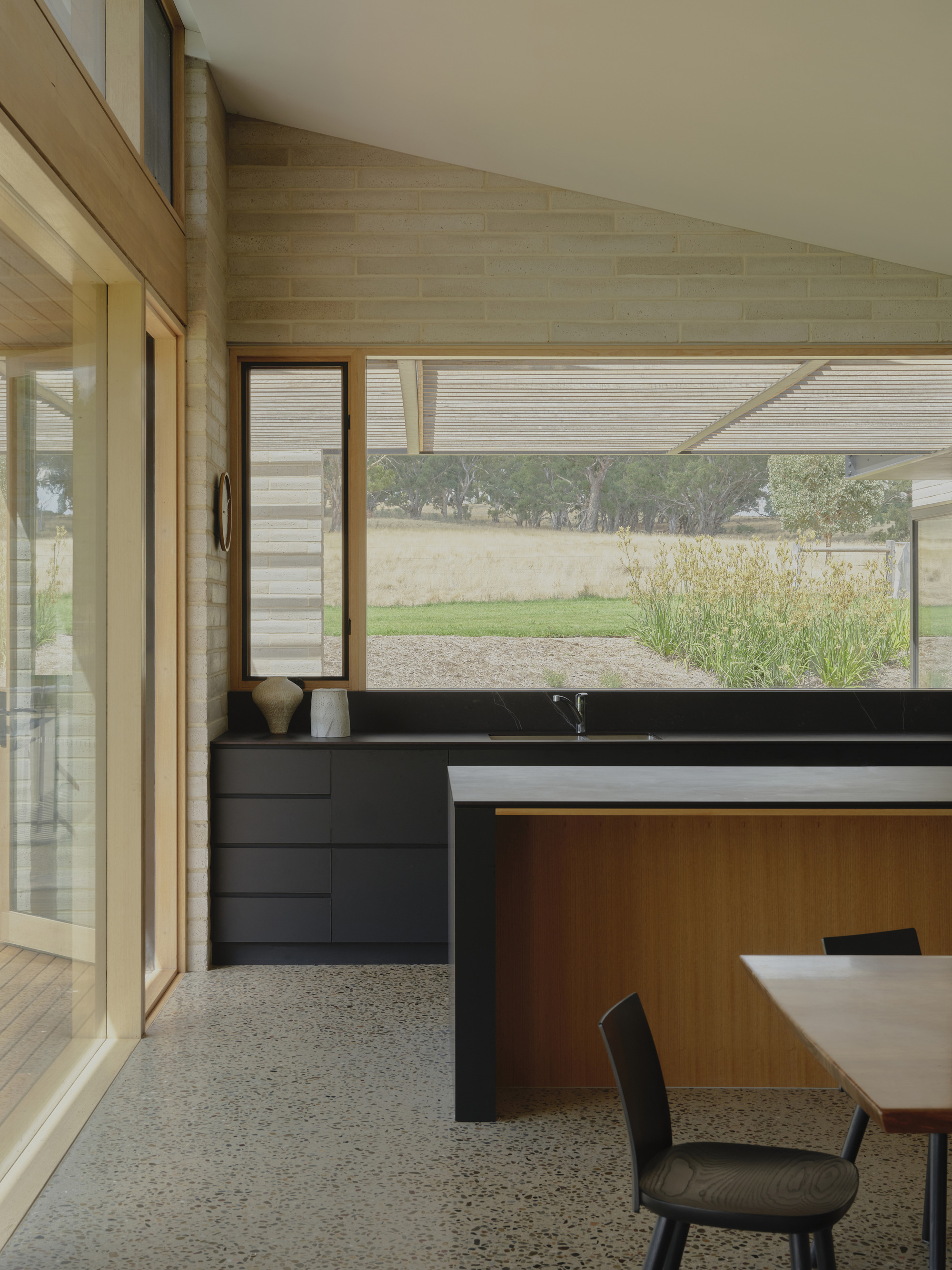 Kitchen with black countertop and timber cabinetry beneath a horizontal clerestory window overlooking the landscape