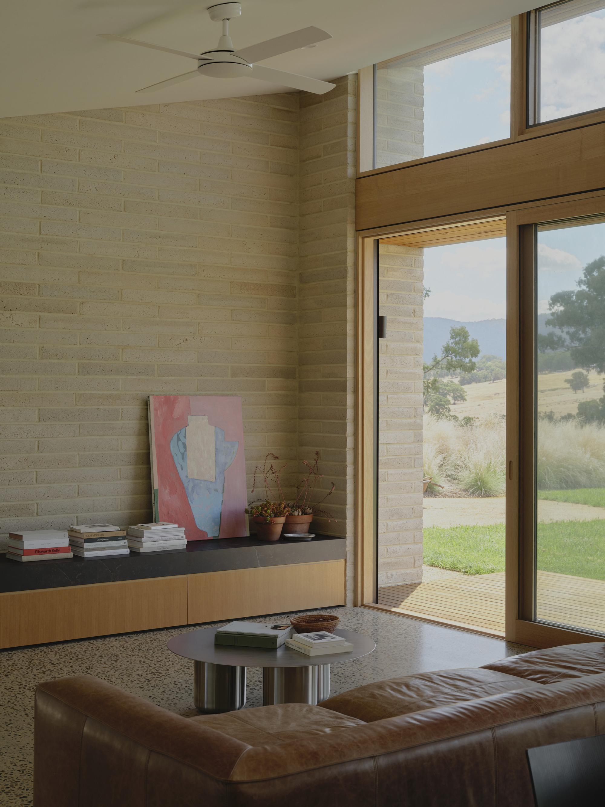 Living room with cream brick wall and full-height glazing opening to the timber deck and hillside