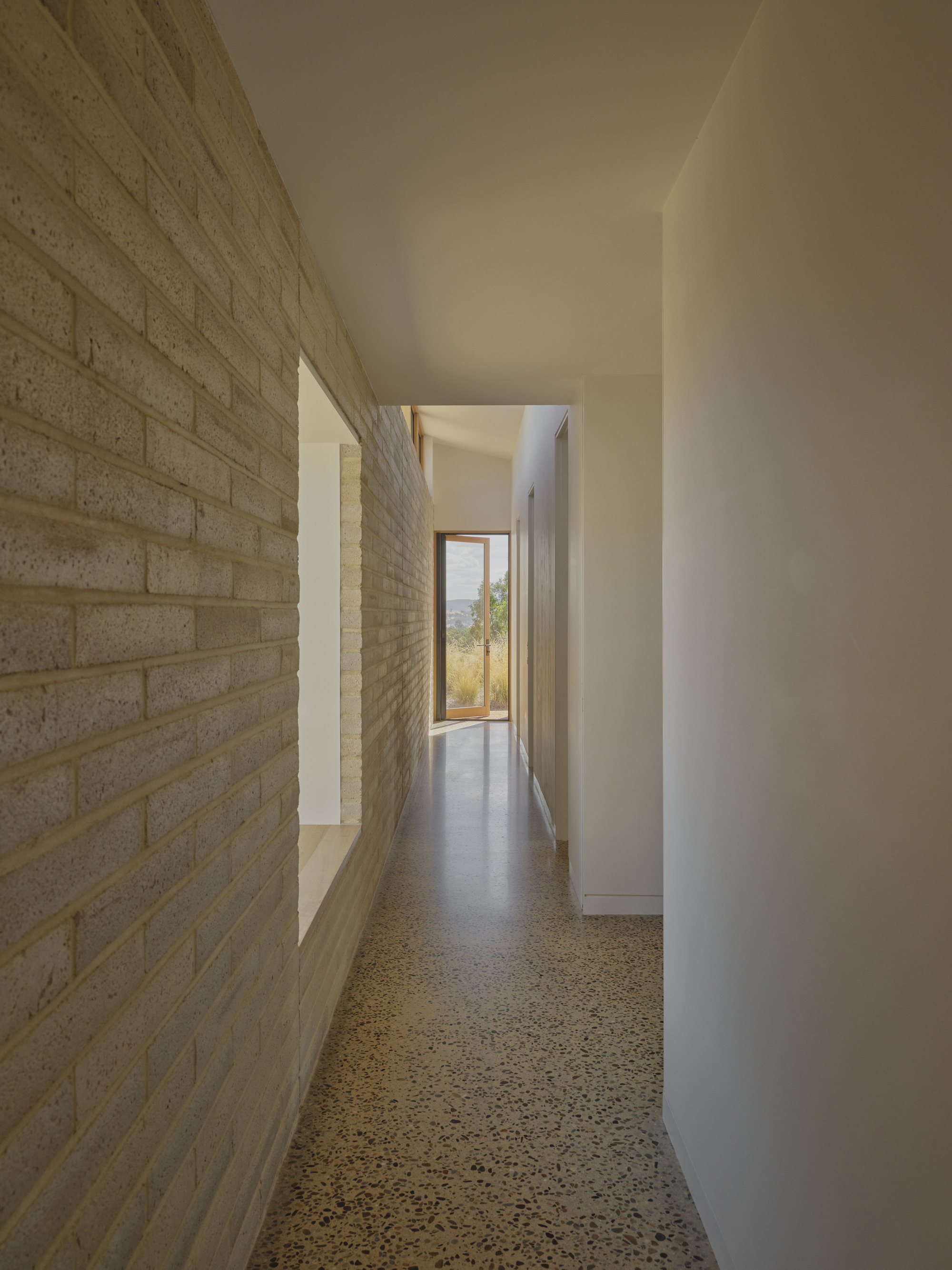 Corridor with polished concrete floor running between cream brick wall and white plaster wall toward framed view