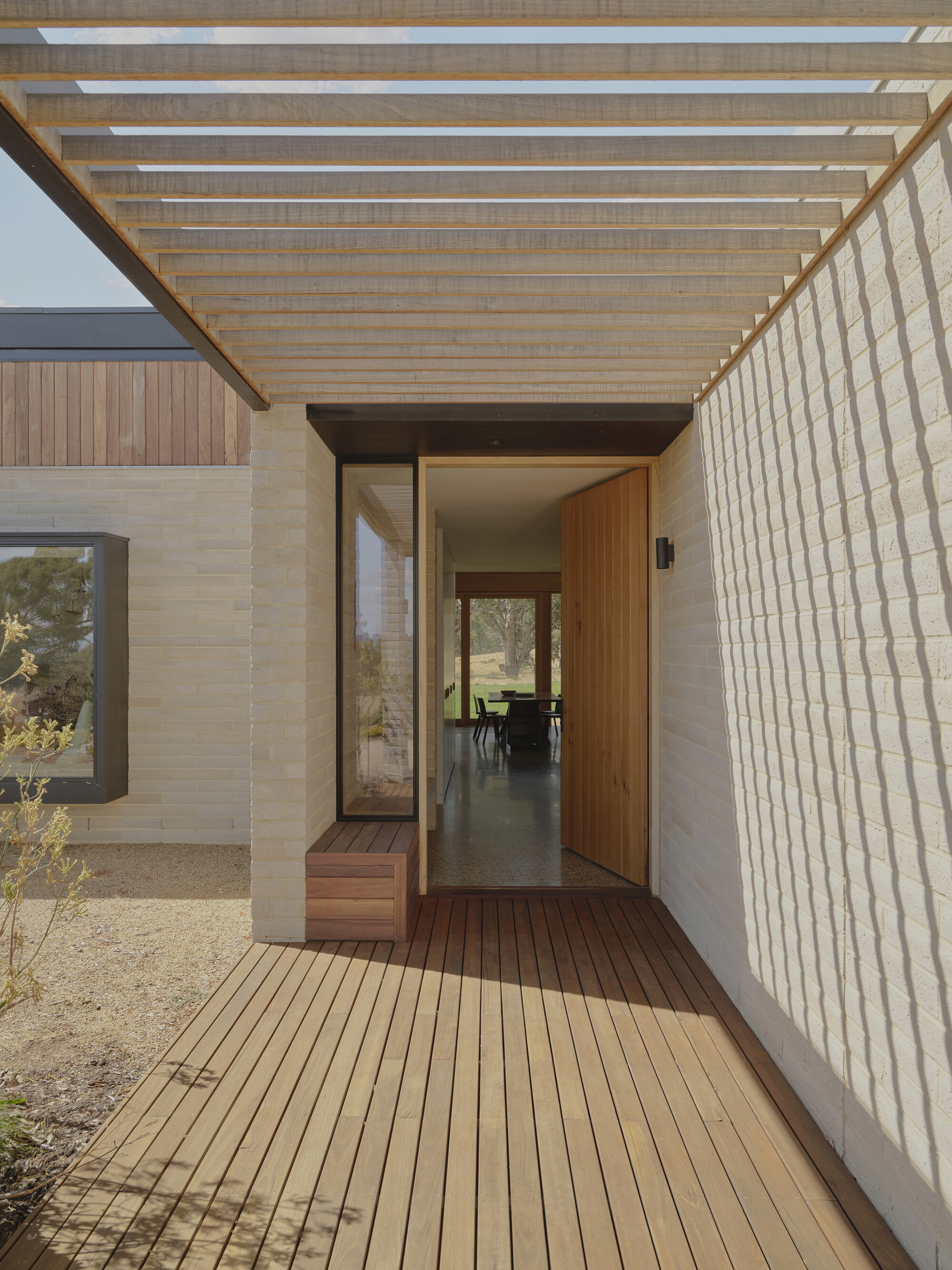 Covered entry porch with timber slatted ceiling, stone walls, and timber decking leading to glazed pivot door