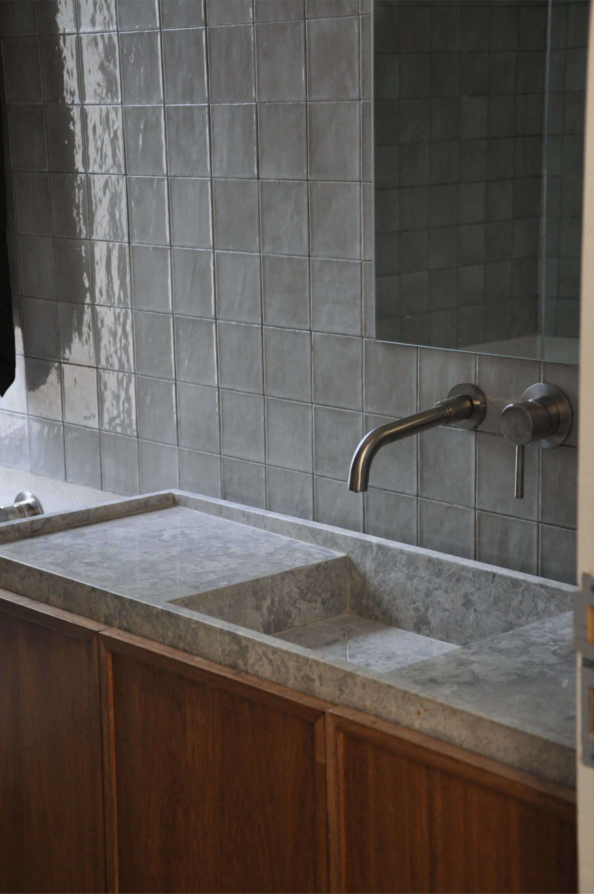 Bathroom vanity with integrated stone sink, glazed tile wall, and wall-mounted bronze faucet