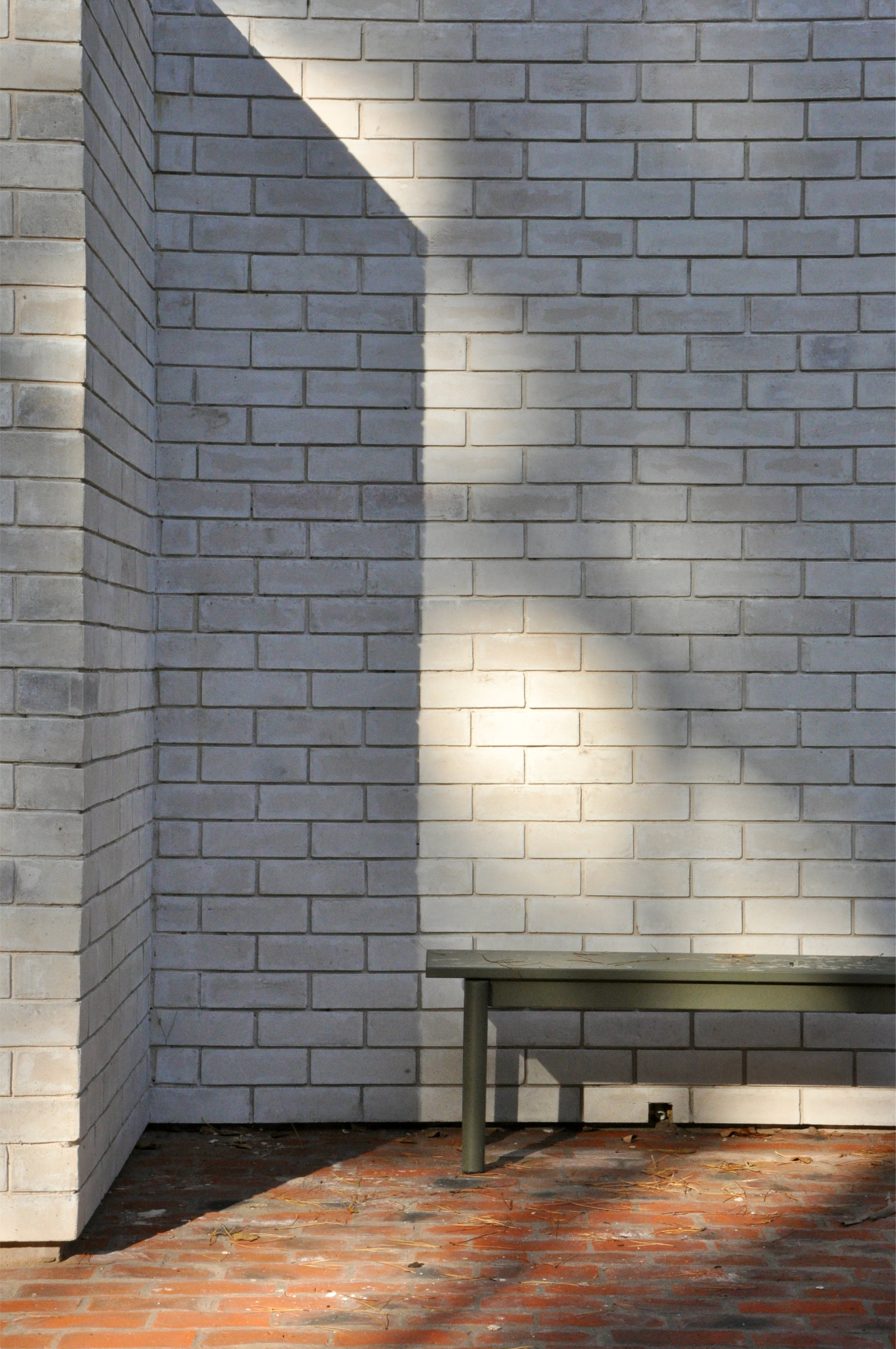 Interior corner with white brick walls and orange tile floor in dappled sunlight