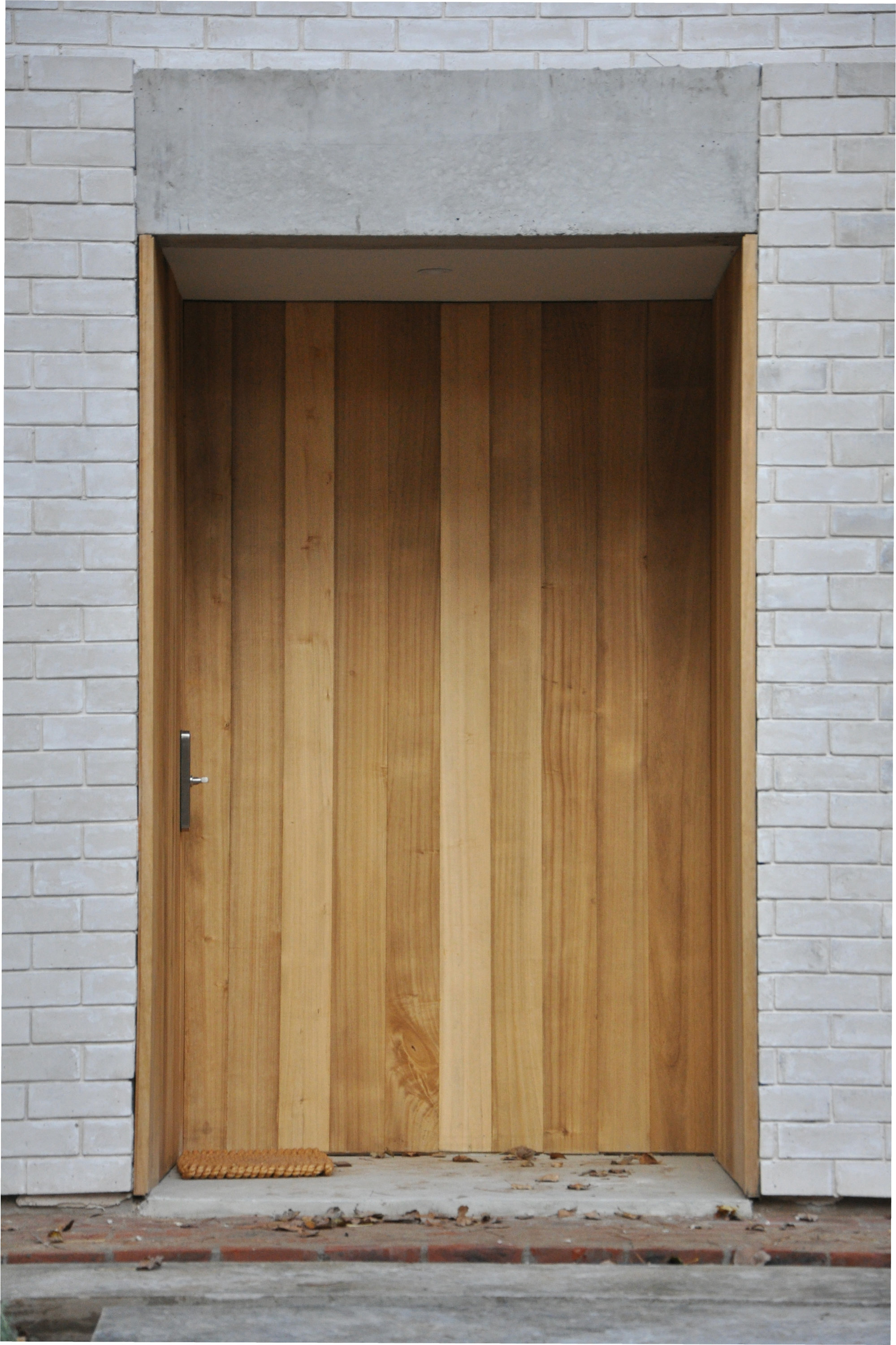 Vertical timber door set within white brick facade and concrete lintel