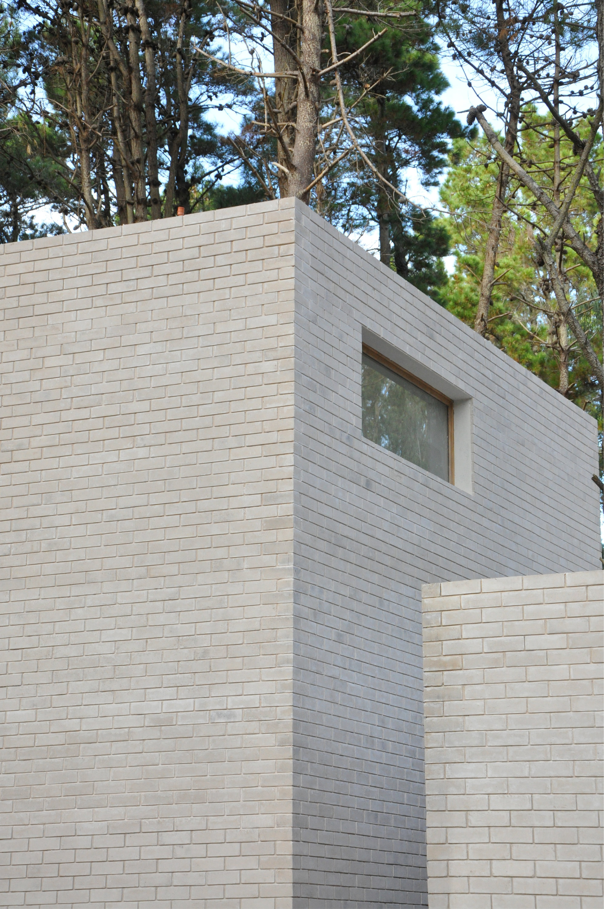Angled white brick volumes meeting at corner with single timber window above