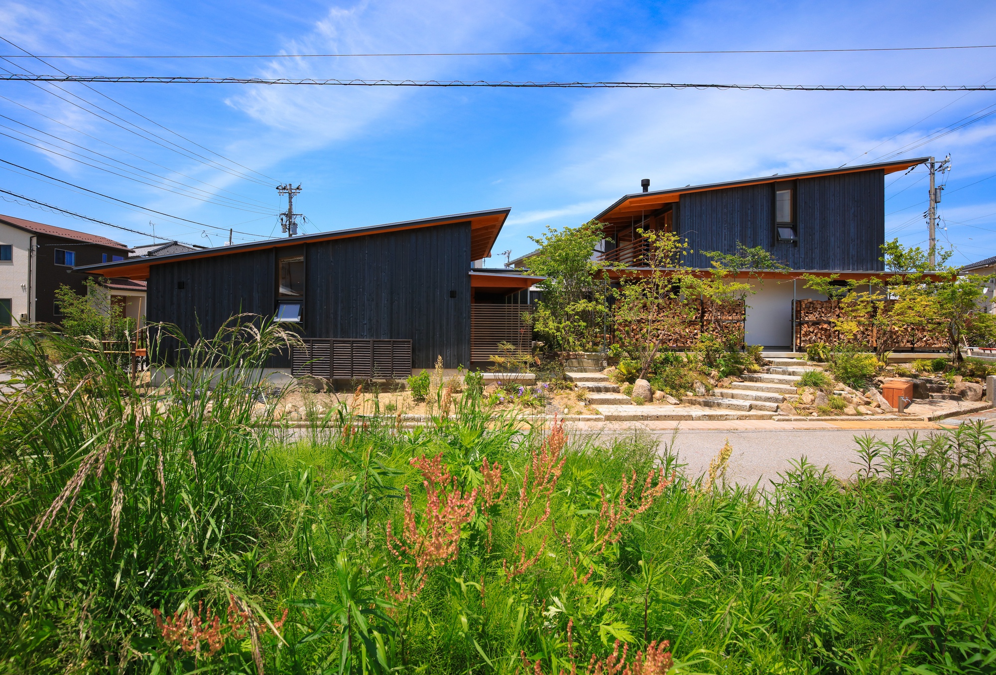 Linked volumes with charred wood siding behind a field of tall grasses under blue sky
