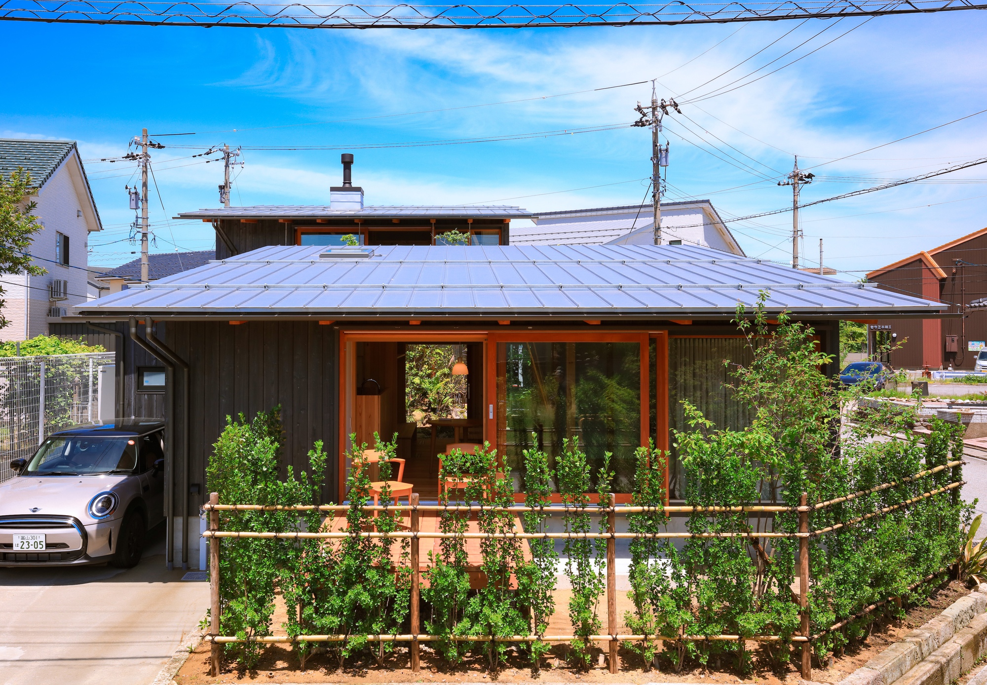 Street facade showing metal standing seam roof above dark timber walls and a carport with vegetable trellis