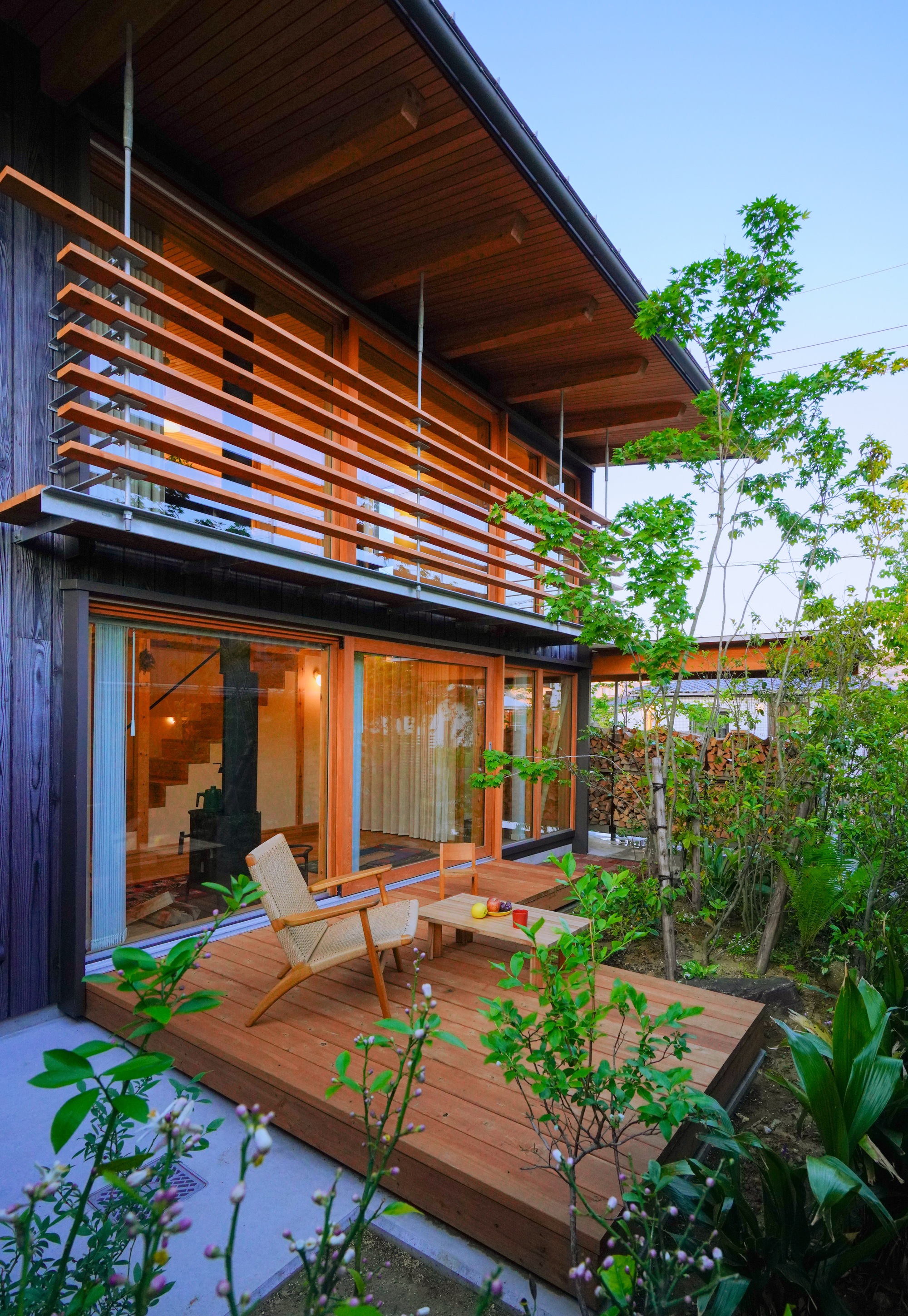 Timber deck terrace with horizontal wood slat screens and glass doors opening to interior at dusk