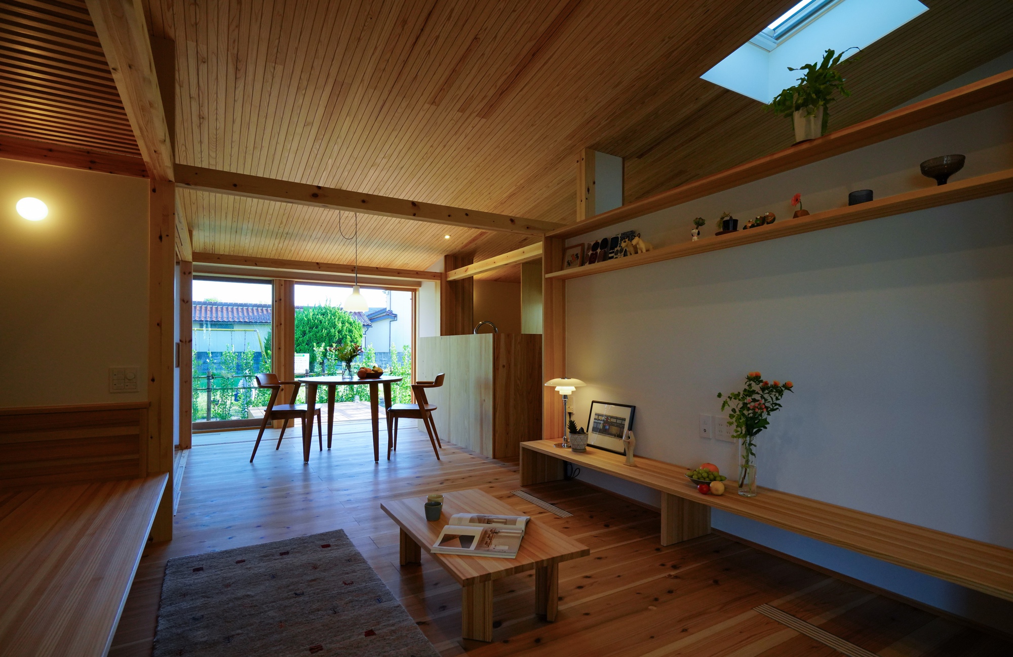 Living room with wood-paneled ceiling and flush threshold opening to outdoor deck and garden beyond