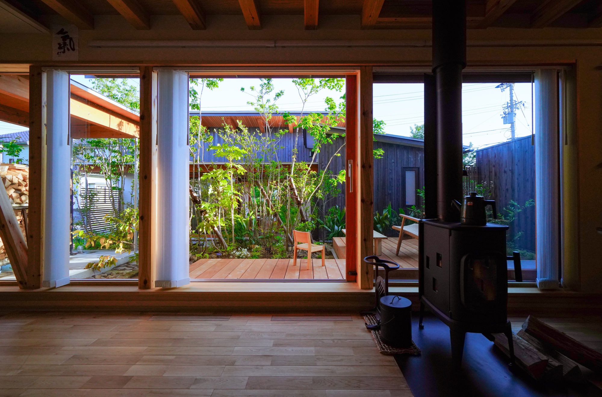 Interior view through timber-framed windows to central courtyard garden with wood stove in foreground