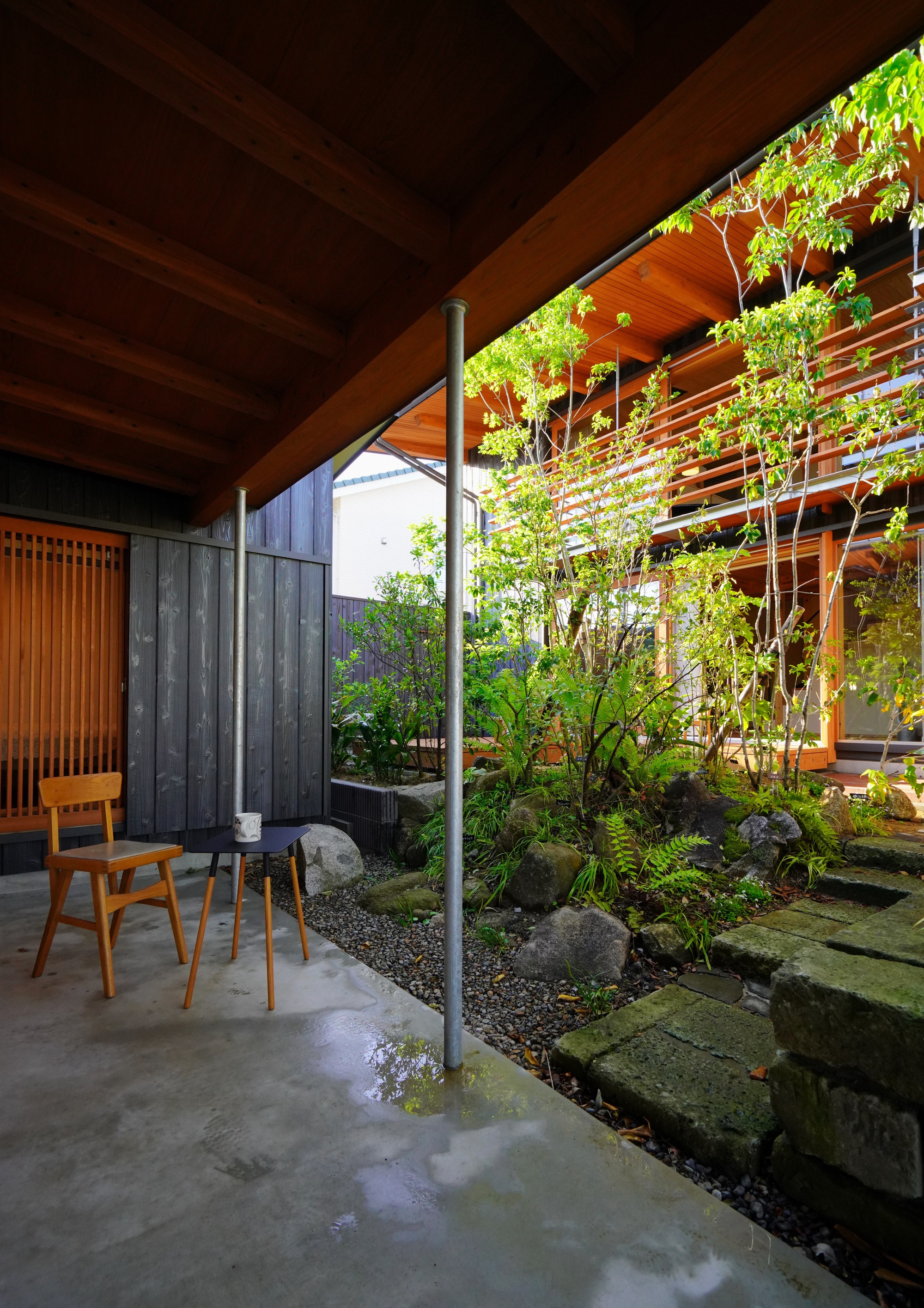 Covered terrace with timber ceiling and slender columns overlooking an interior courtyard garden with stepping stones