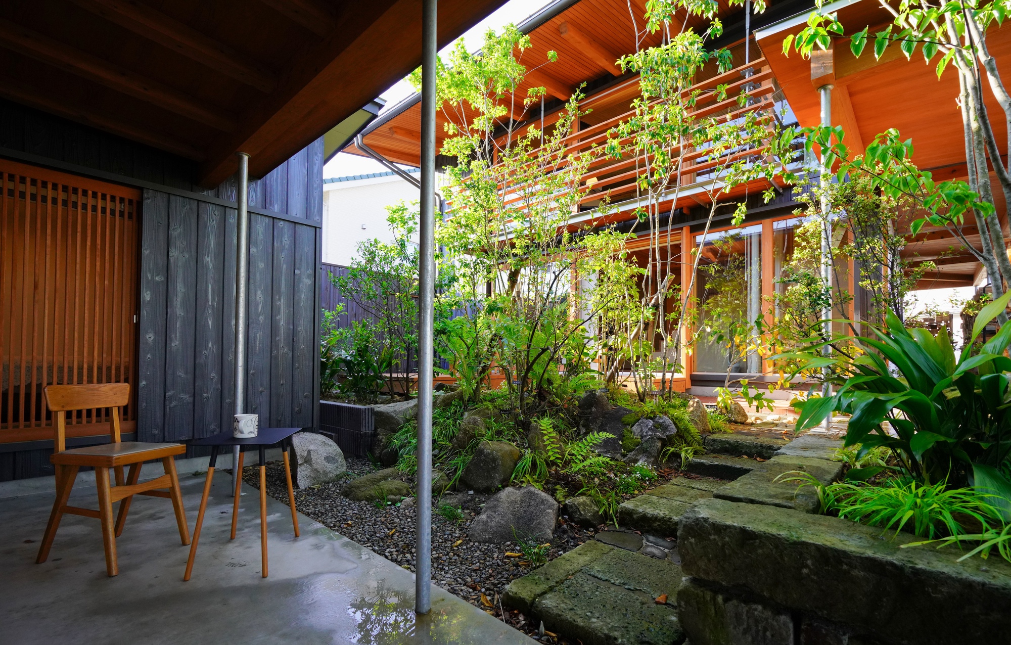 Concrete patio beneath exposed timber rafters looking into a planted courtyard with moss-covered stone pavers