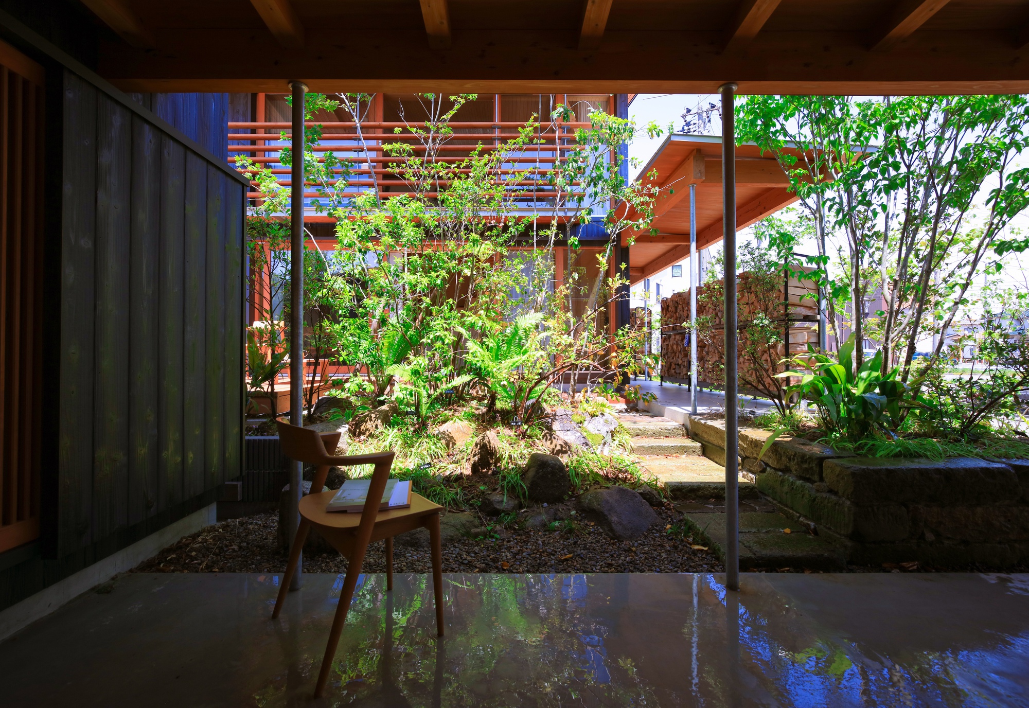 Glass-enclosed courtyard garden with stone path and tropical plantings beneath timber-clad linking structures