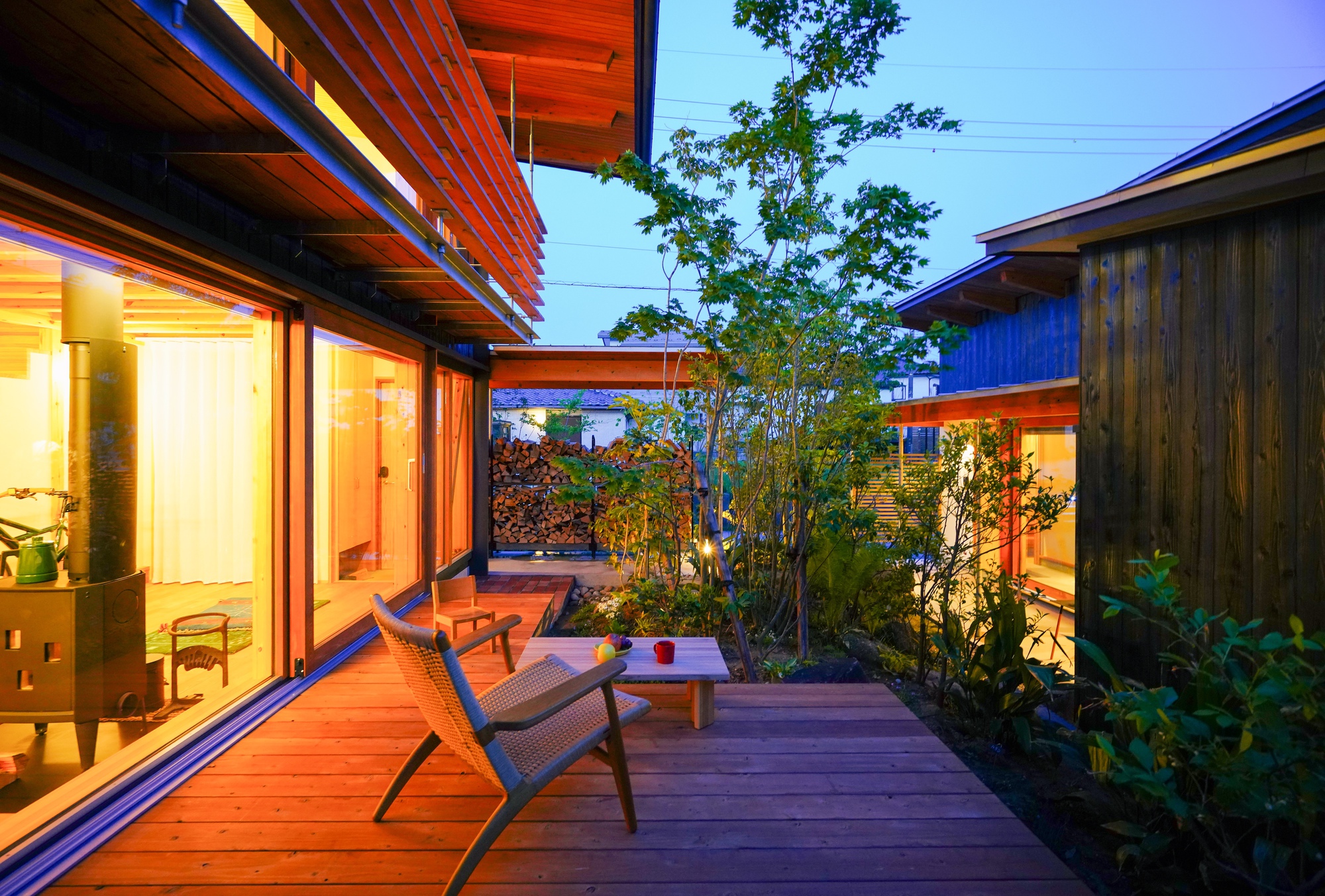 Timber deck terrace at twilight overlooking central courtyard garden with illuminated interiors beyond