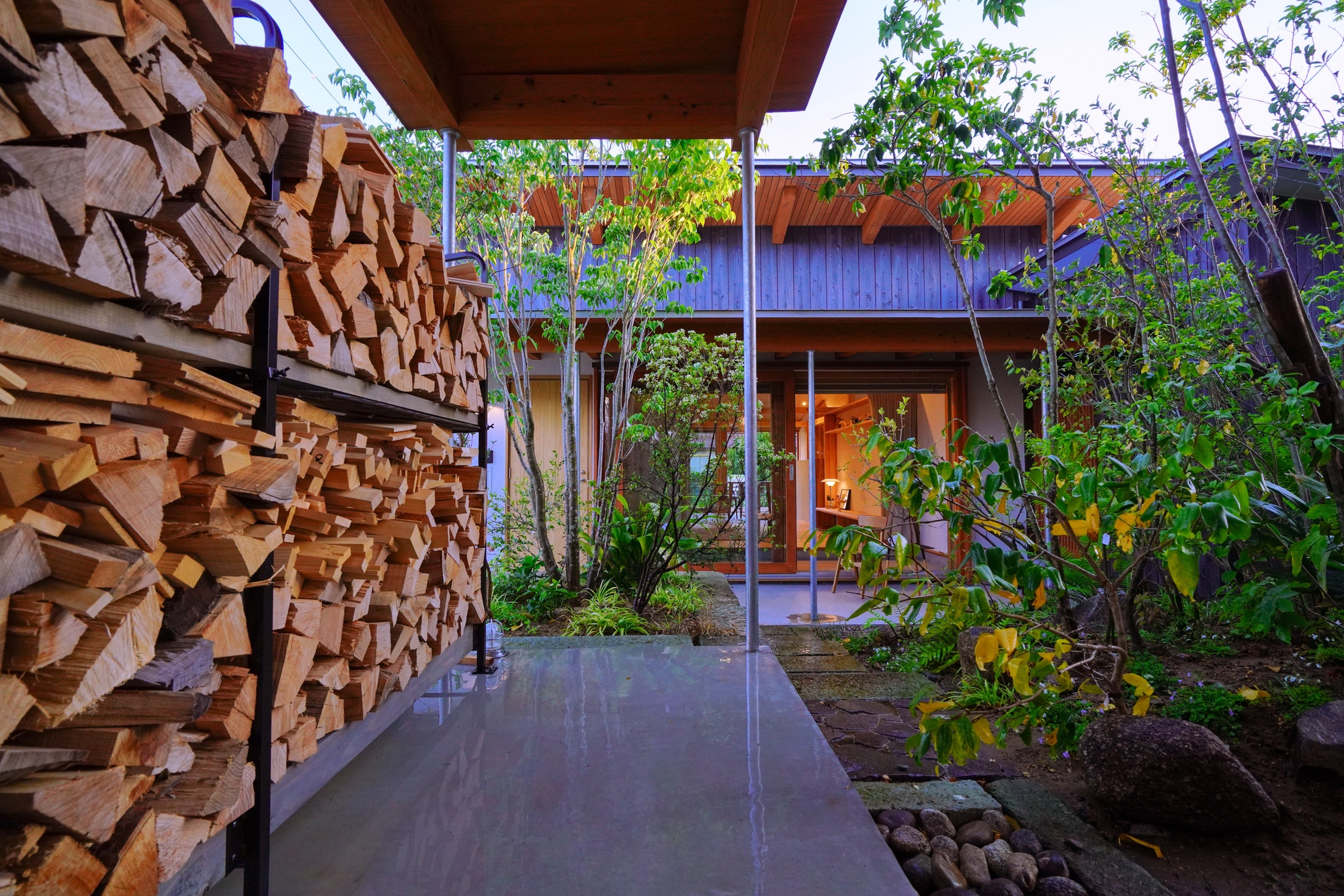 Stacked firewood wall beside concrete walkway leading to courtyard garden at dusk