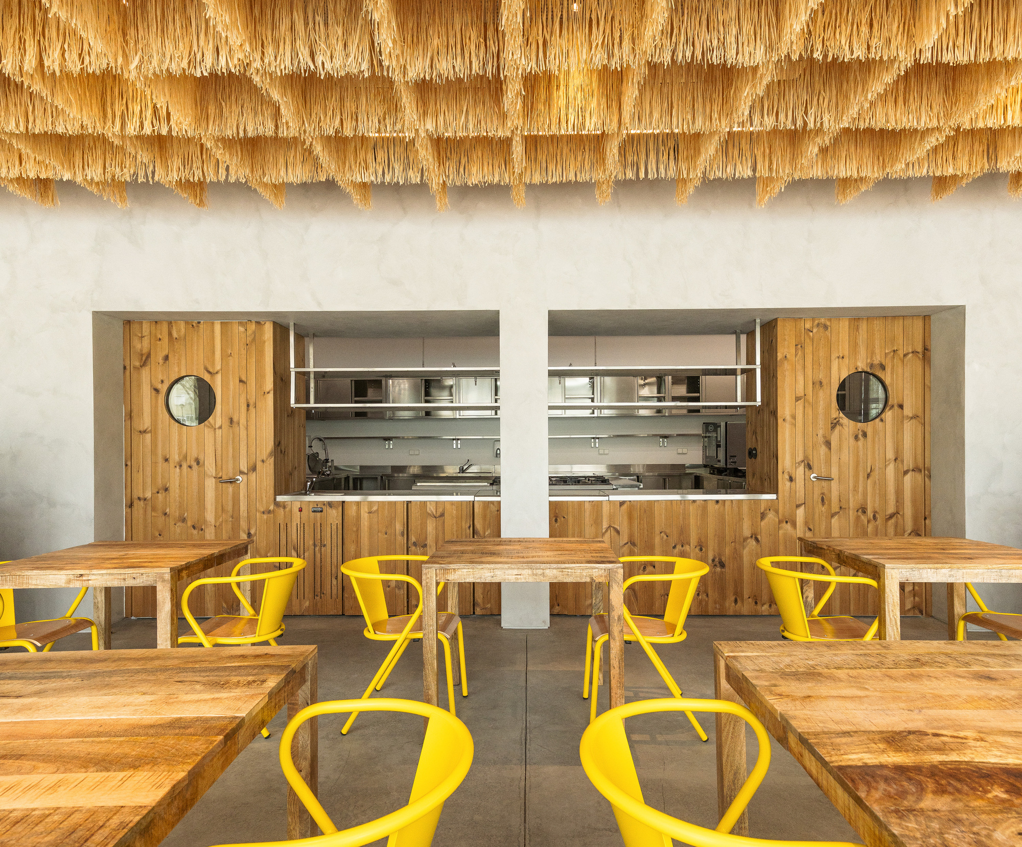 Symmetrical timber kitchen alcoves with circular portholes beneath fringed raffia ceiling edge