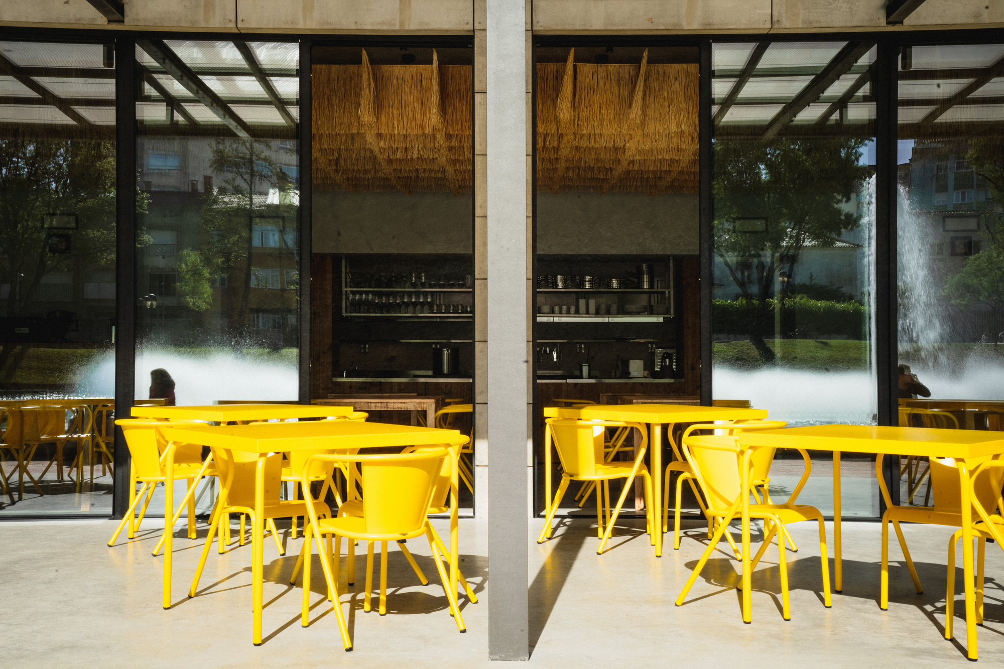 Outdoor terrace seating with yellow furniture under concrete structural frame in afternoon sunlight