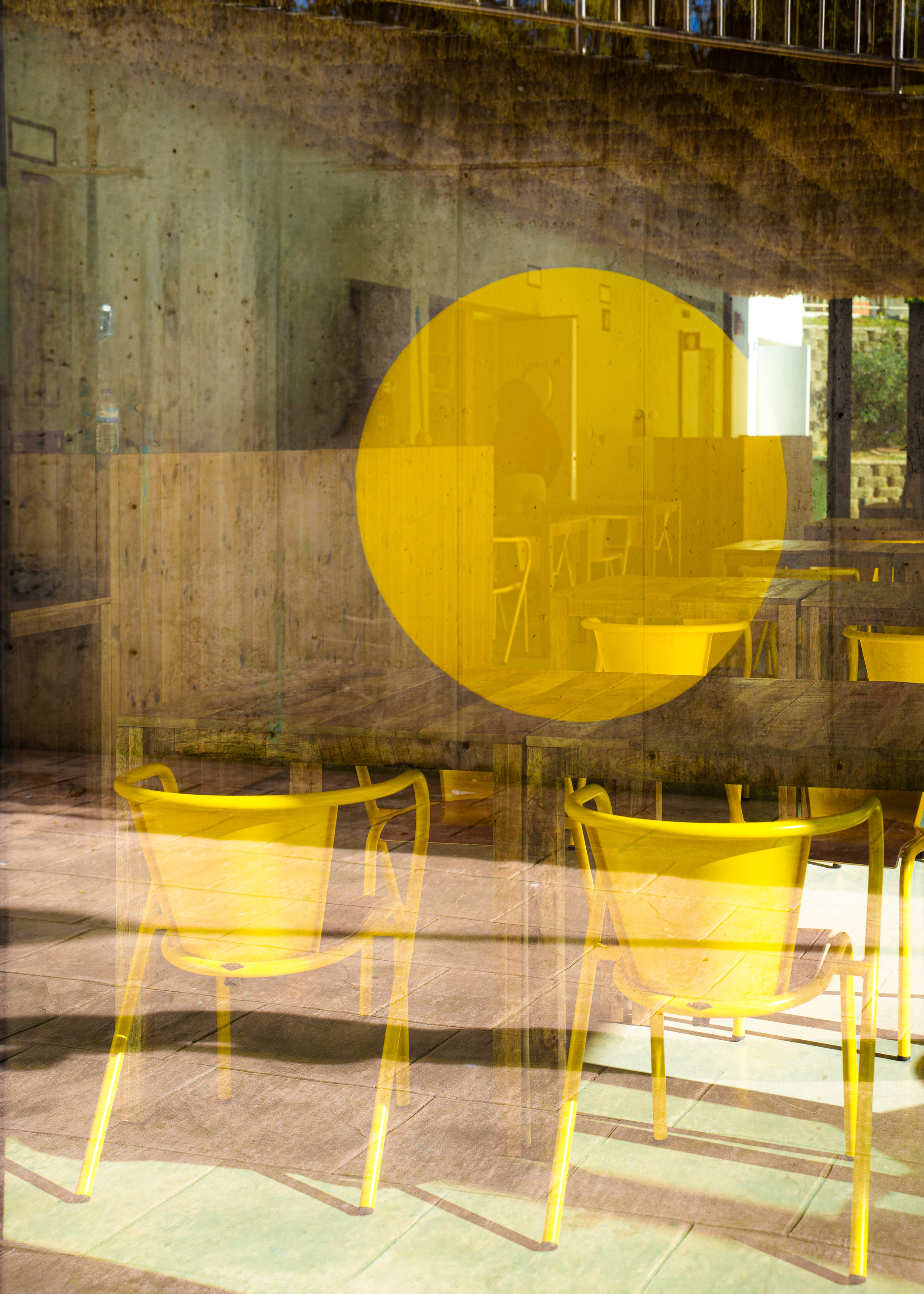 Yellow chairs behind glass with circular yellow graphic at a concrete wall