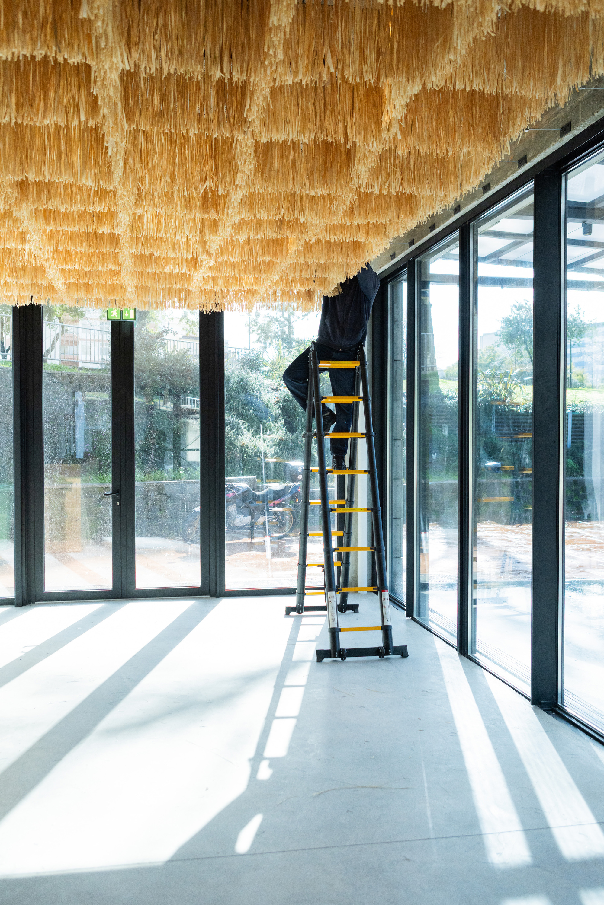 Interior corridor with layered ceiling panels and full-height glazing casting diagonal shadows on polished concrete floors