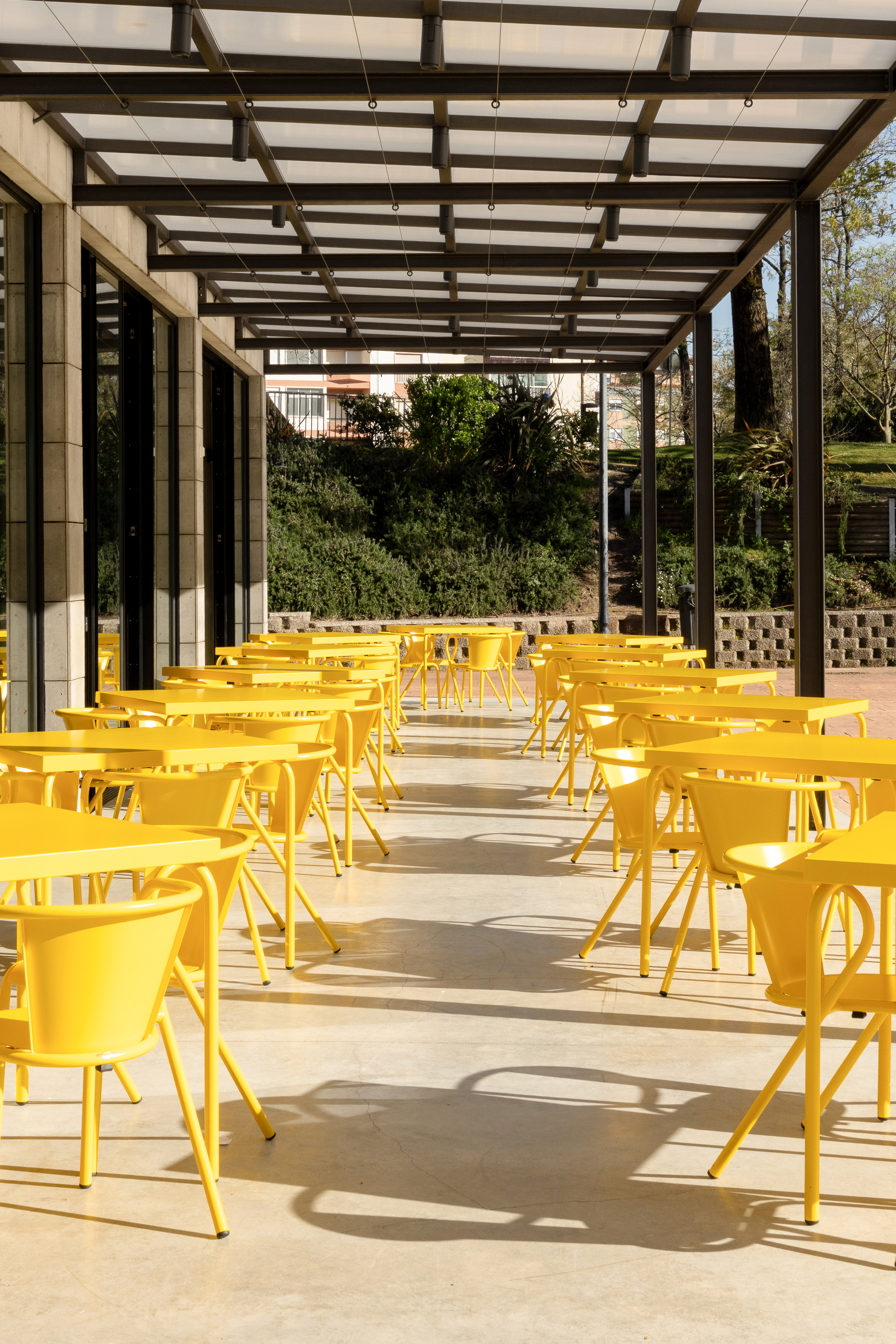 Covered terrace with steel frame pergola, yellow metal tables and chairs, and a vertical garden backdrop