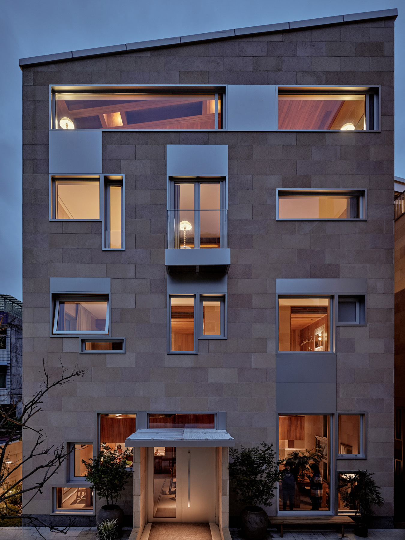Street facade with grey block cladding and scattered windows illuminated at dusk