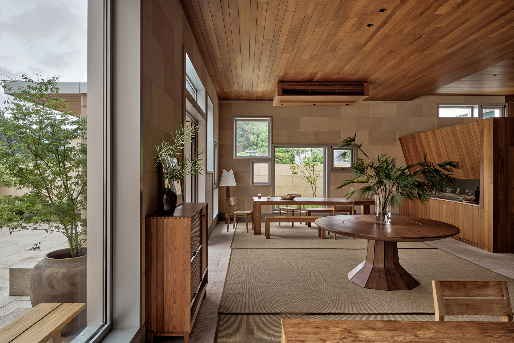 Living space with timber plank ceiling and terrace view through floor-to-ceiling glass doors