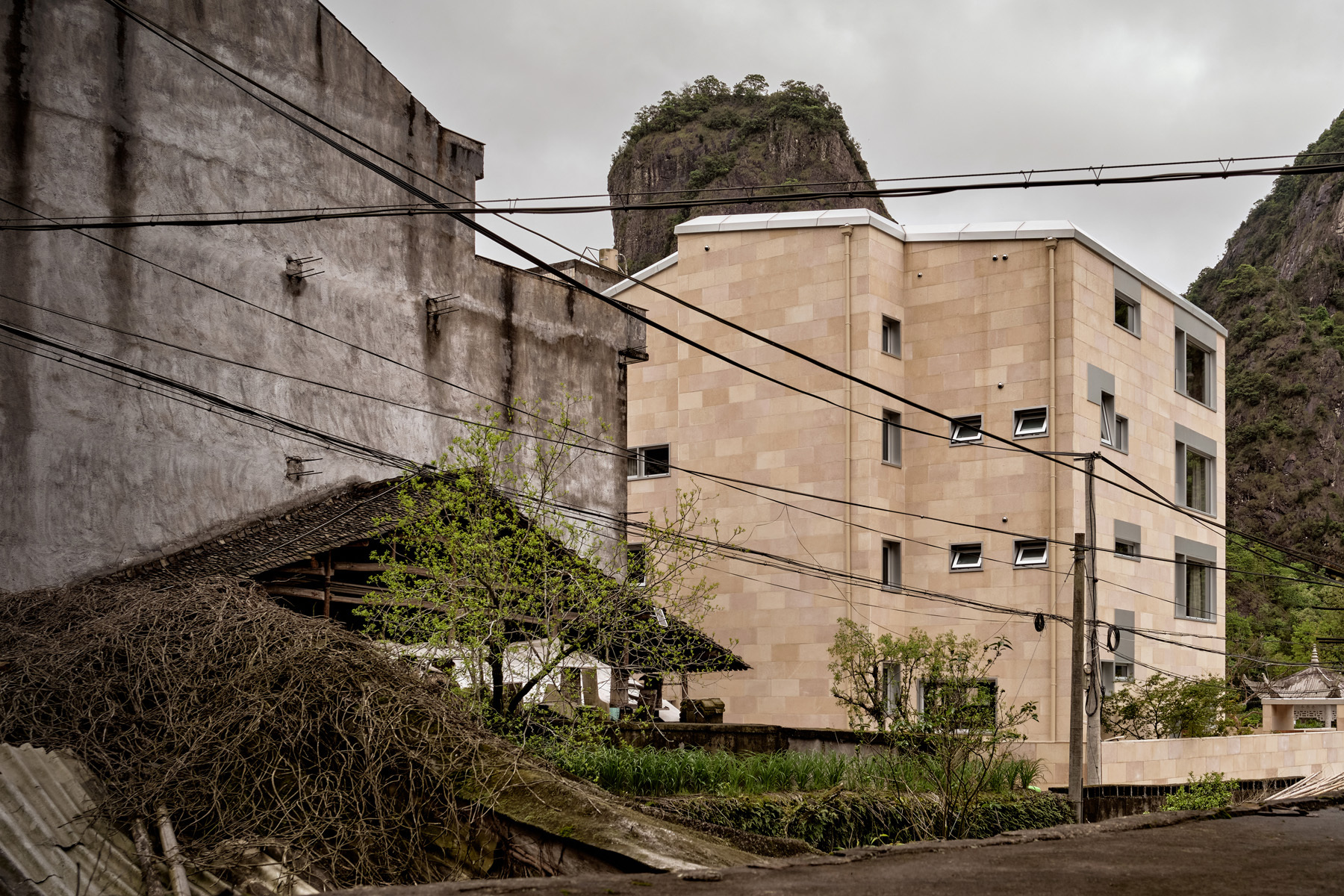 Street view of the multi-story sandstone facade with overhead power lines and a rocky hillside backdrop