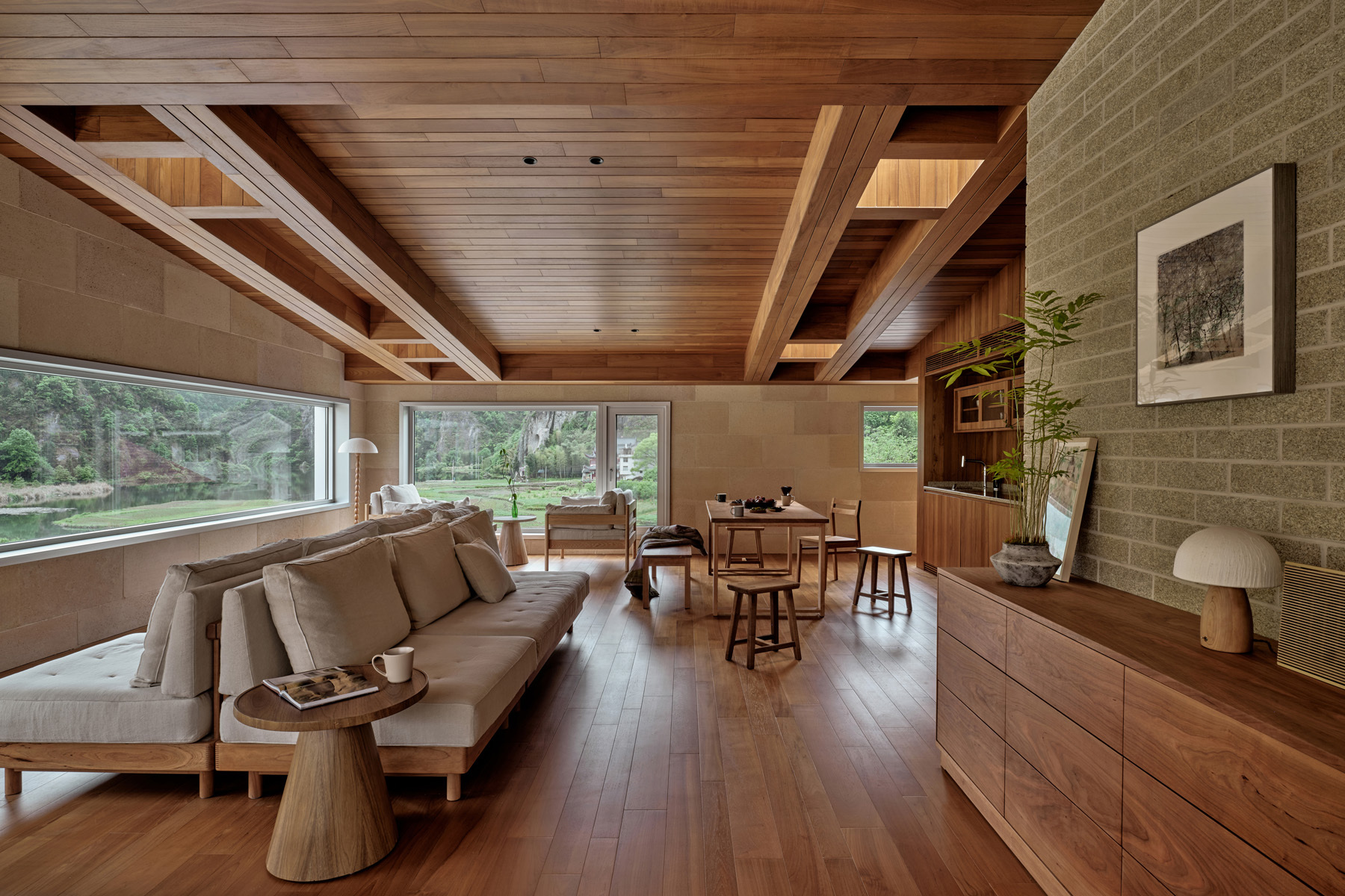 Living room with exposed timber beams and wide horizontal windows framing views of the garden beyond