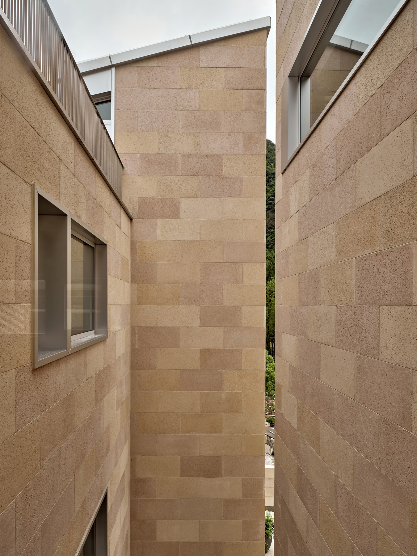 Narrow courtyard between sandstone block walls with glimpse of green hillside under an overcast sky