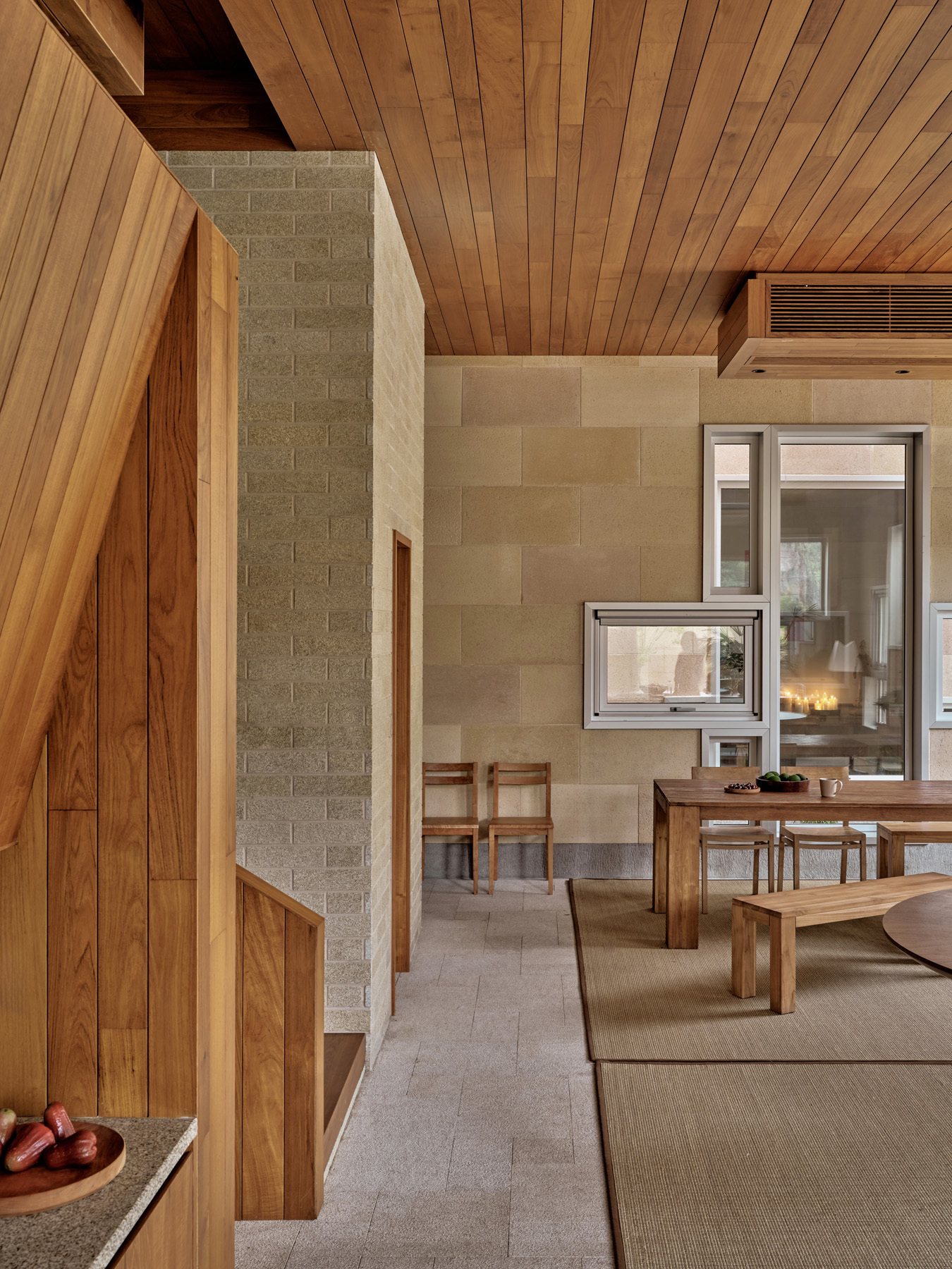 Living area with timber ceiling, concrete block walls and a double-sided fireplace connecting to the dining space