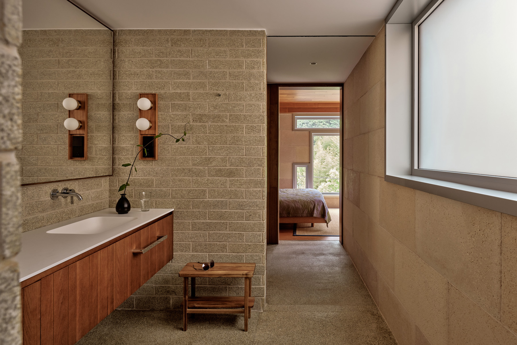 Bathroom with concrete block wall, timber vanity and open doorway revealing a bedroom beyond