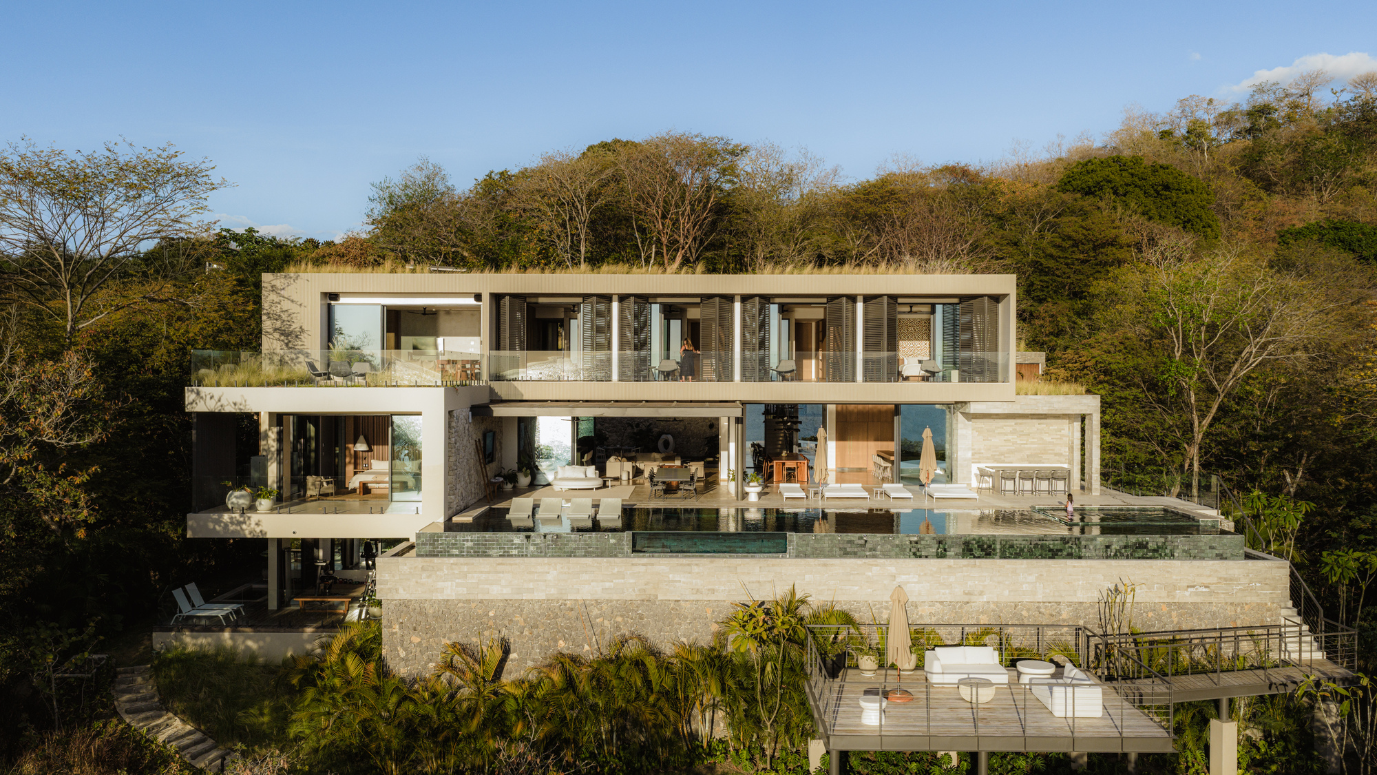 Rear elevation showing stacked concrete terraces with full-height glazing and infinity pool overlooking the forest