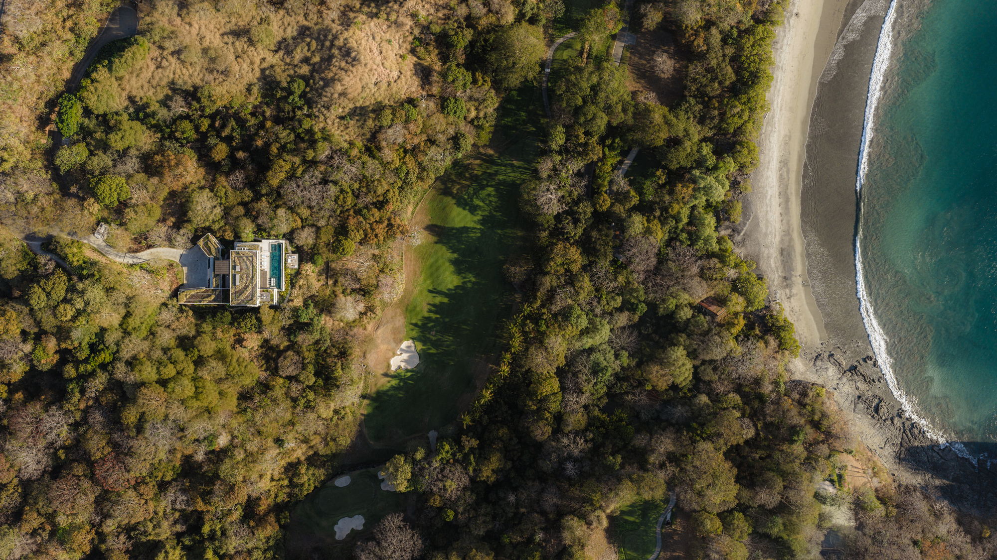 Drone view of the residence set among dense tree canopy between forest and coastline