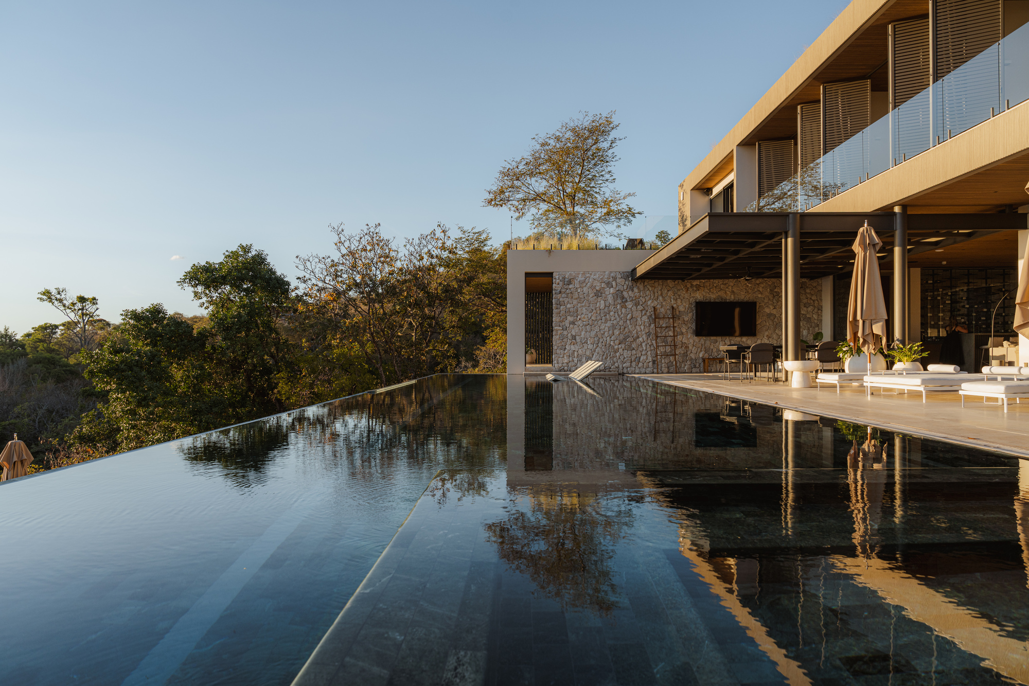Infinity pool reflecting stone walls and timber soffits at dusk overlooking the treetops