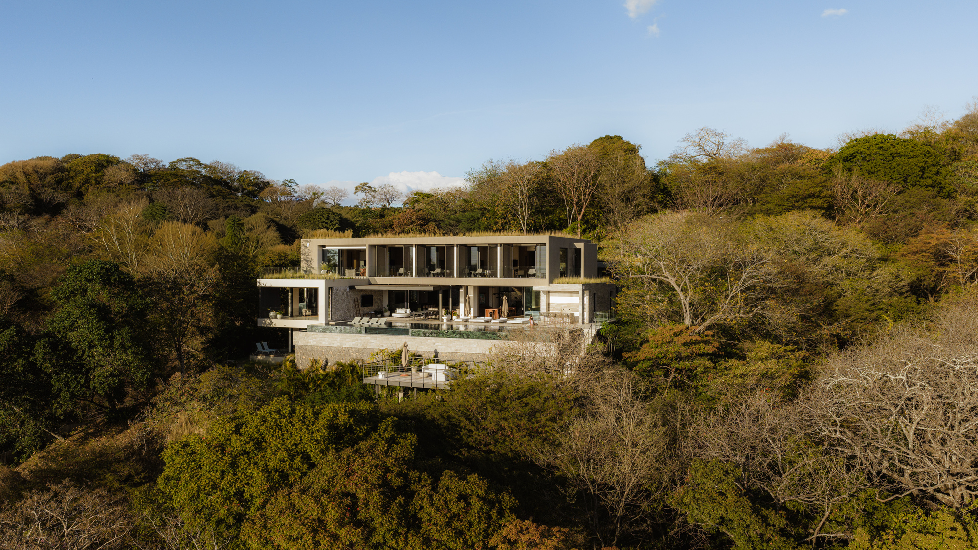 Two-story facade with horizontal bands of glazing and terrace embedded in tropical hillside vegetation